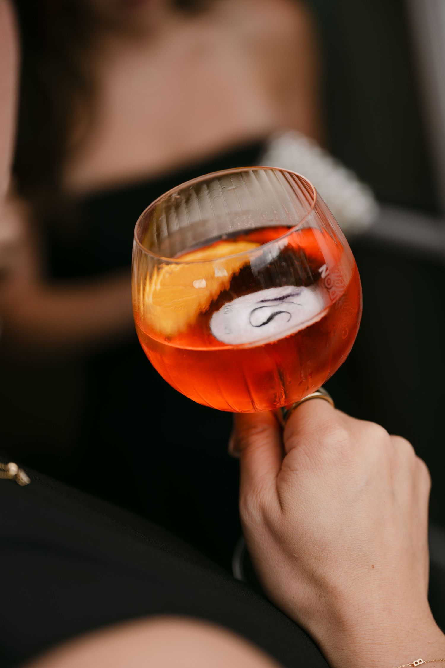Close-up of a hand holding a stemless wine glass with an orange Aperol Spritz cocktail garnished with an orange slice.