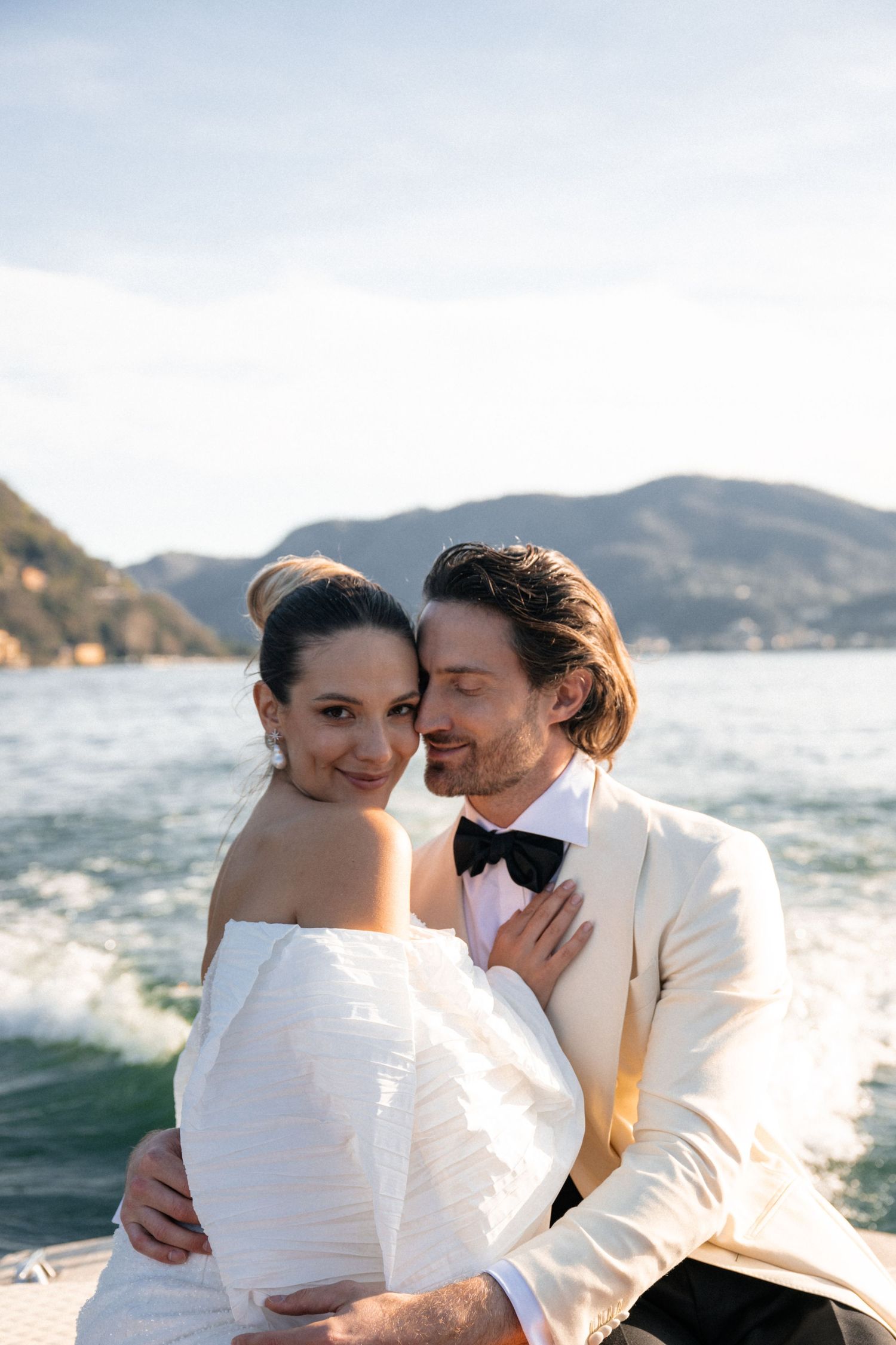 Romantic portrait of bride and groom embracing on a boat with Lake Como mountains behind them.