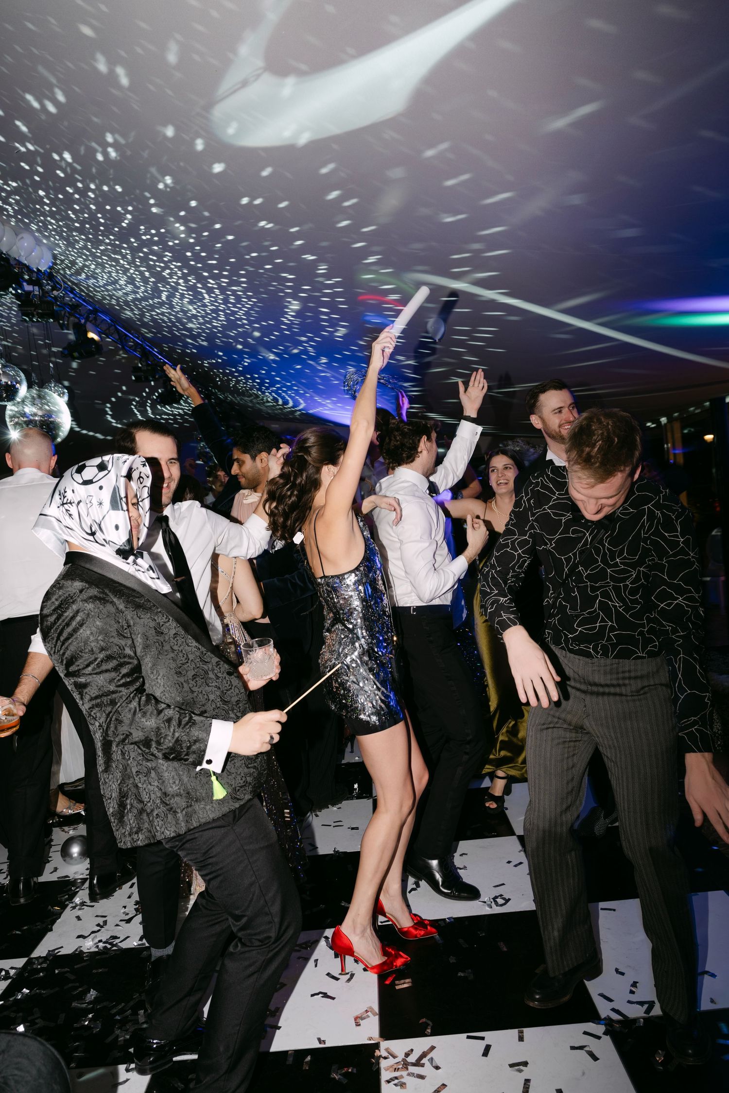 Wedding guests dancing with confetti falling on black and white dance floor at lively reception party.