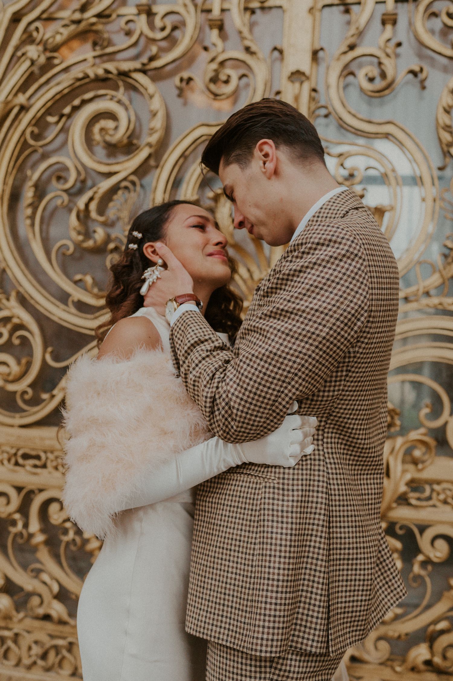 Intimate wedding portrait of couple embracing against ornate golden gates.