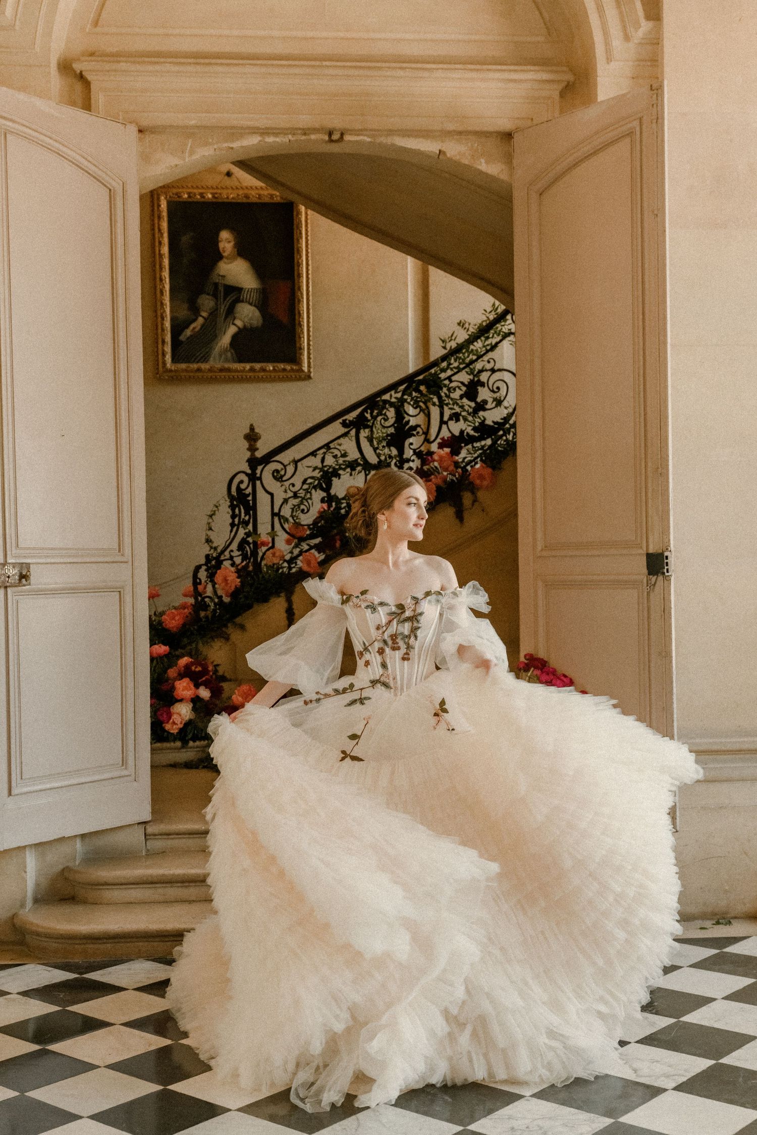 A bride twirls in a voluminous white ballgown near an ornate staircase with classical decor.