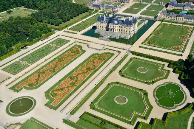 Aerial view of a grand French chateau with elaborate geometric gardens and ornate landscaping patterns.