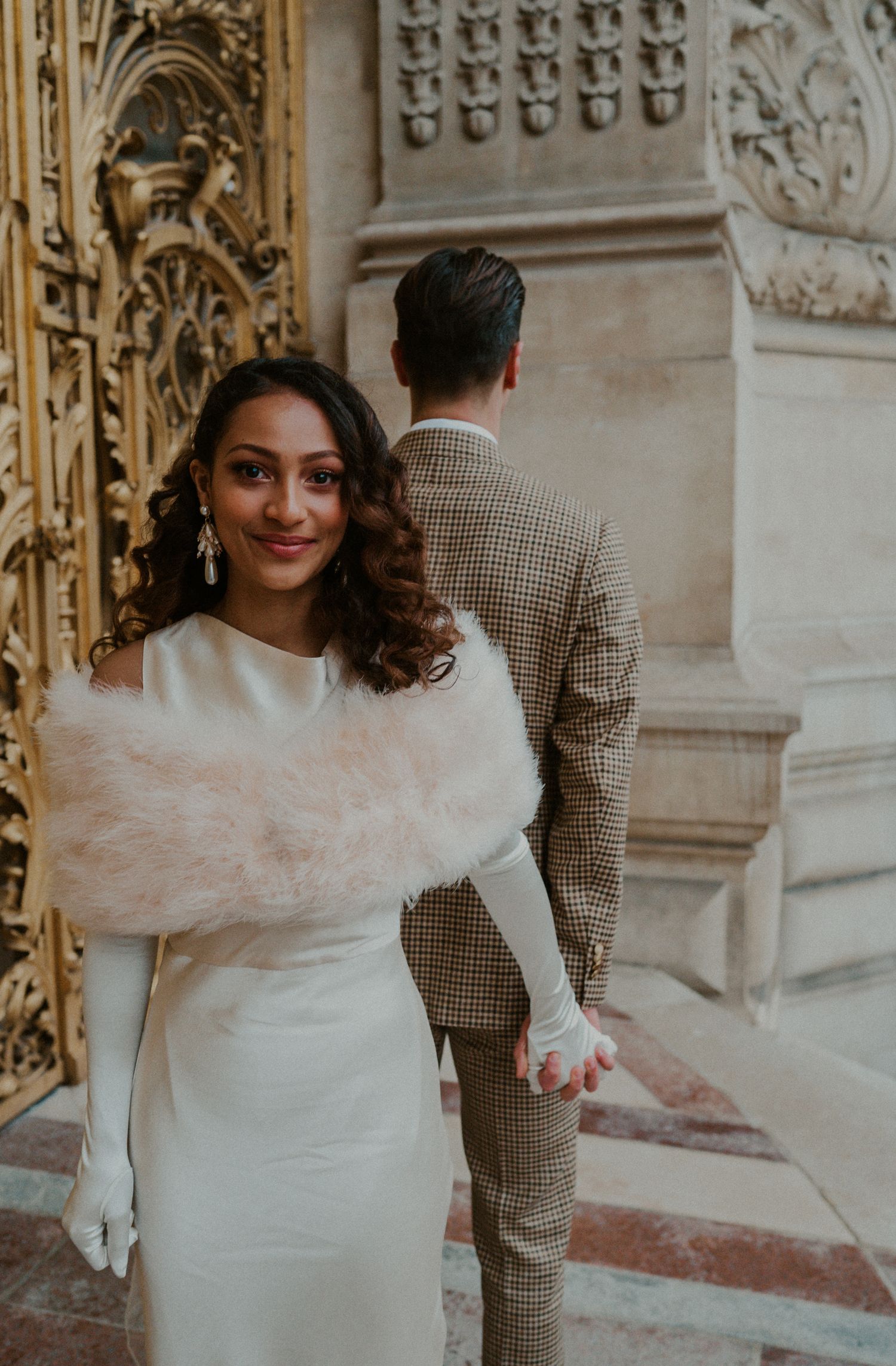 Wedding portrait of a couple in front of ornate gold gates with the bride in white and groom in plaid.