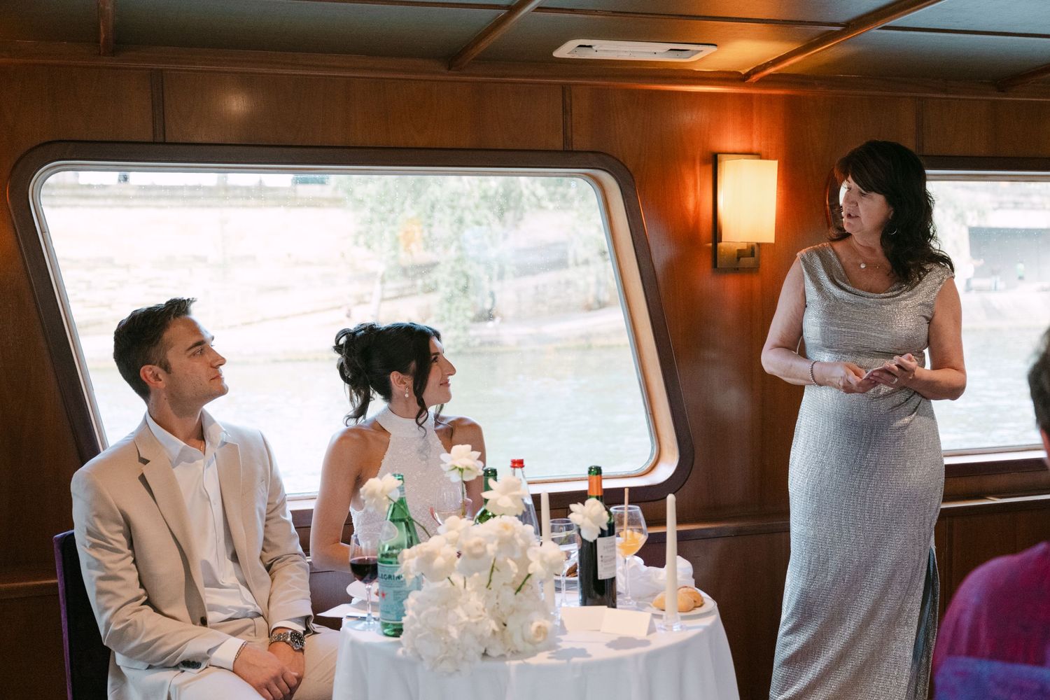 Wedding reception celebration aboard a yacht with guests mingling and a white floral centerpiece.