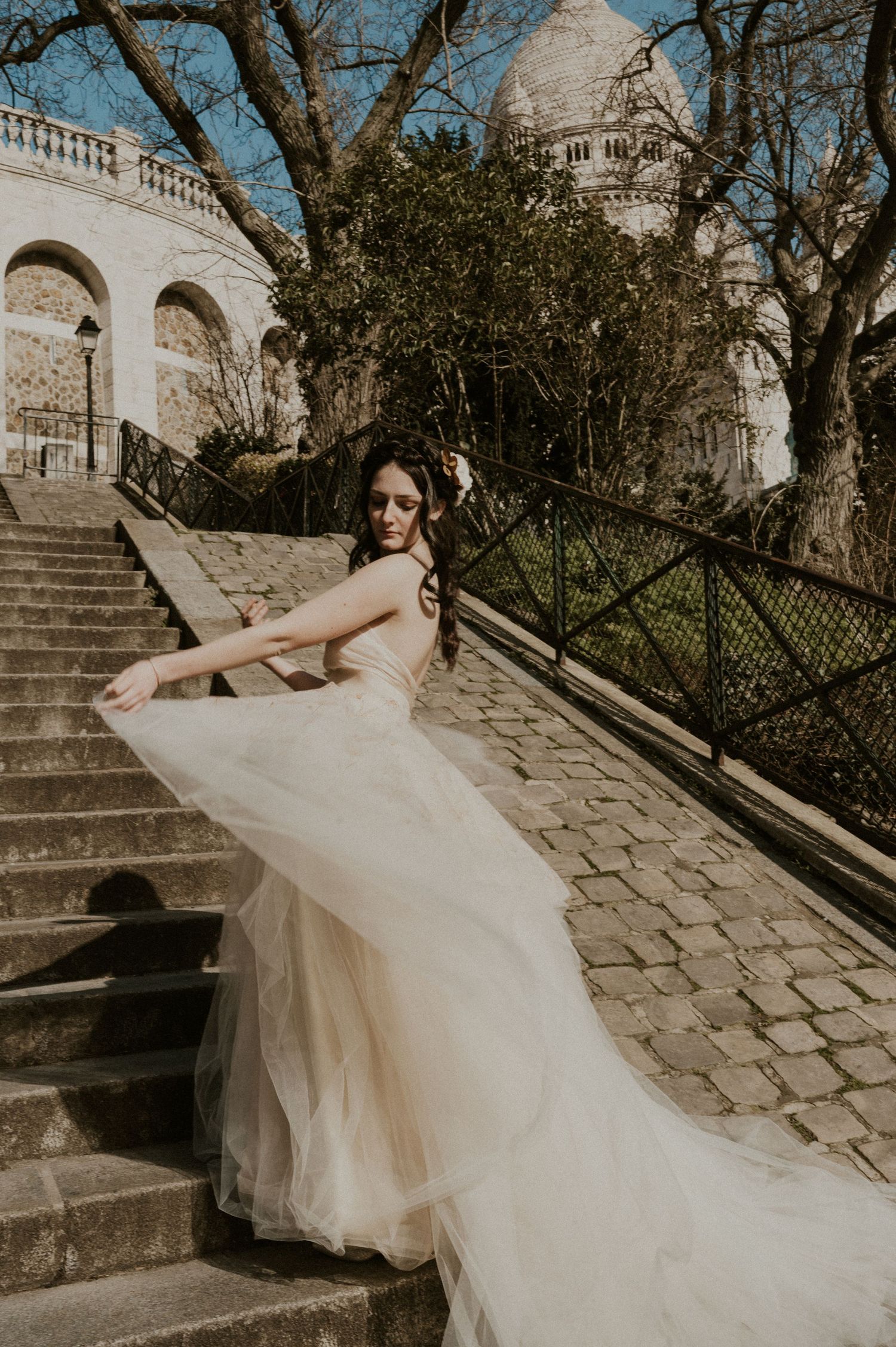 Elegant bridal portrait with flowing dress train on stone steps near Sacré-Cœur basilica.