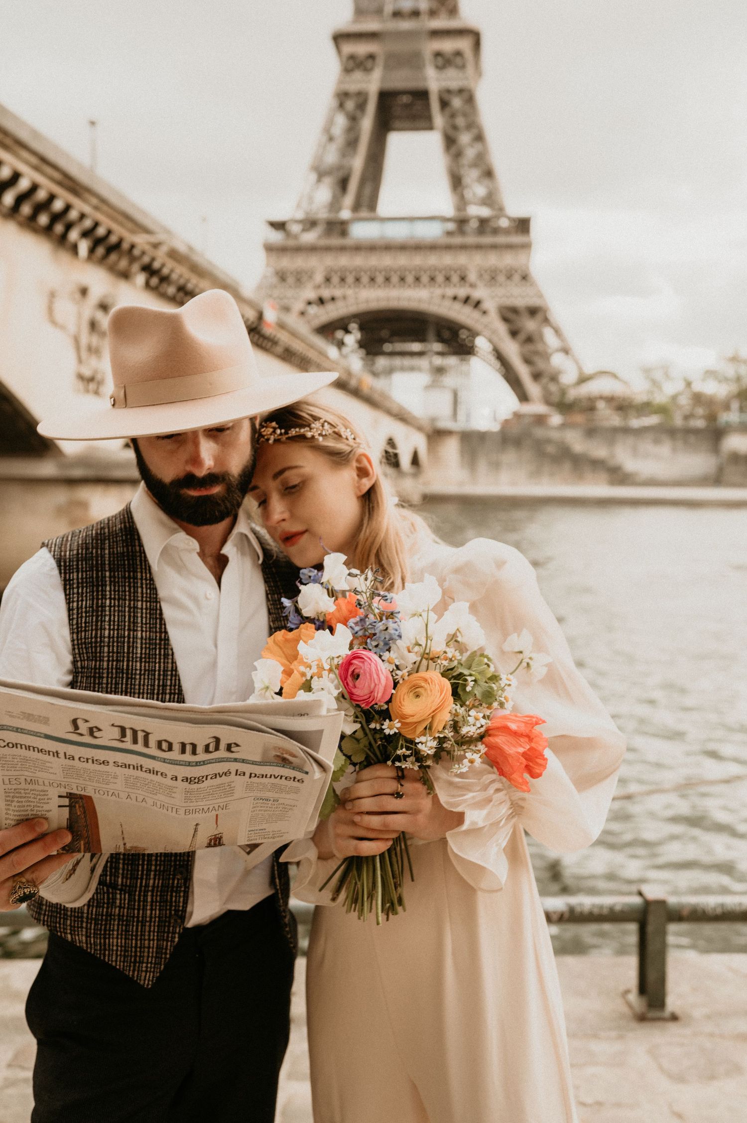 Romantic couple in vintage attire sharing tender moment near Eiffel Tower with bouquet and newspaper.