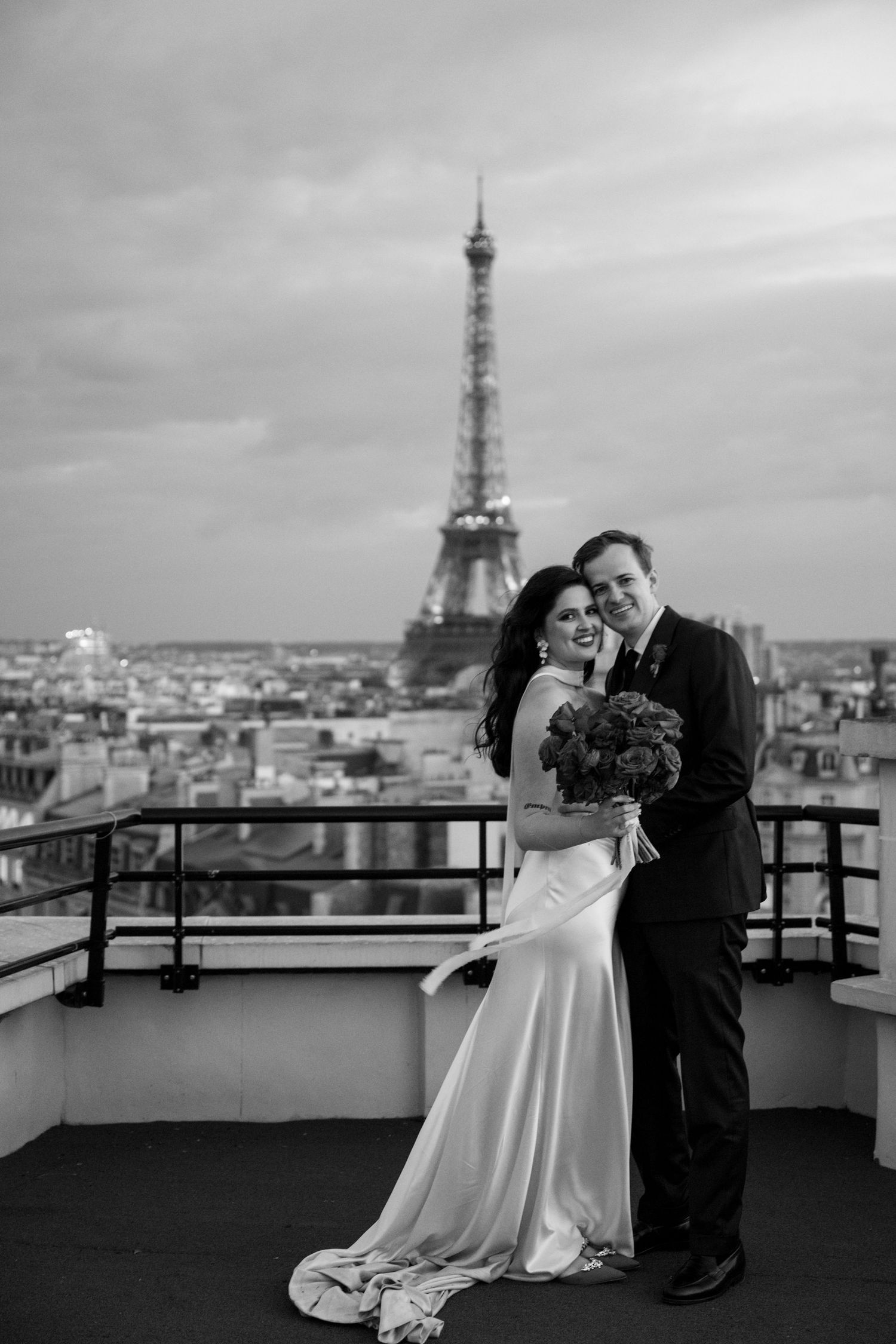 Elegant black and white portrait of newlyweds embracing on a Parisian rooftop with the Eiffel Tower in the background.