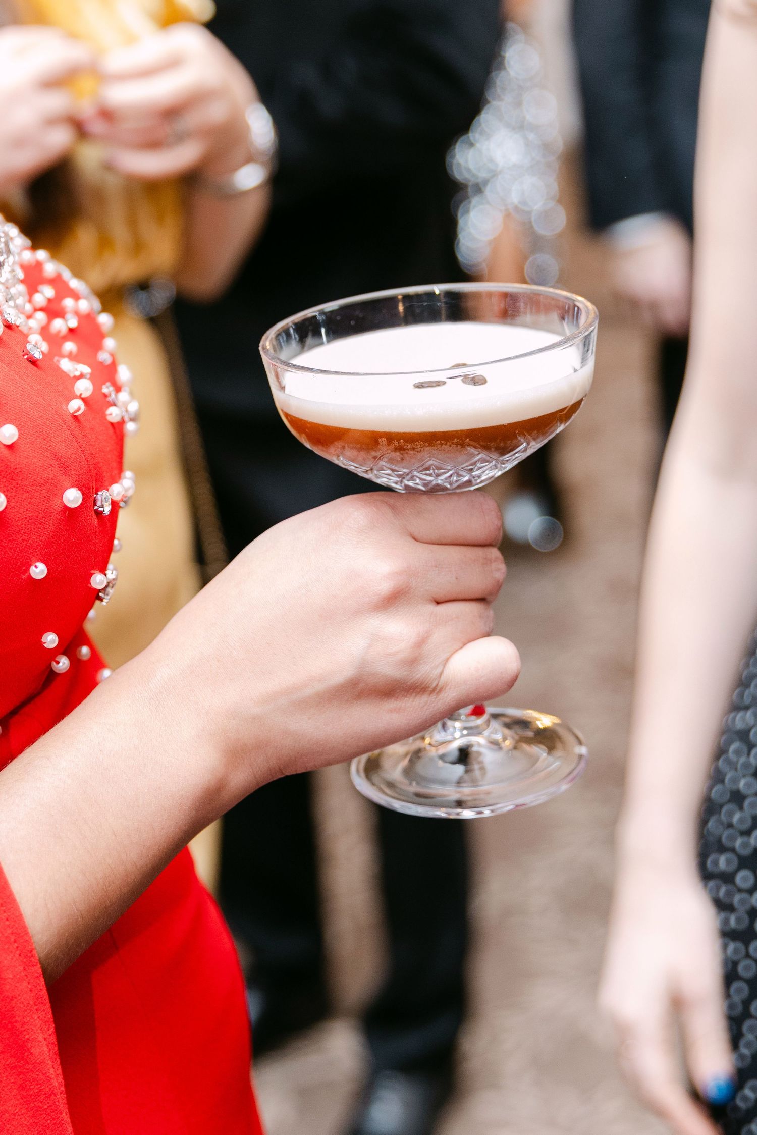 Guest in red beaded dress holding crystal coupe glass with espresso martini at wedding.