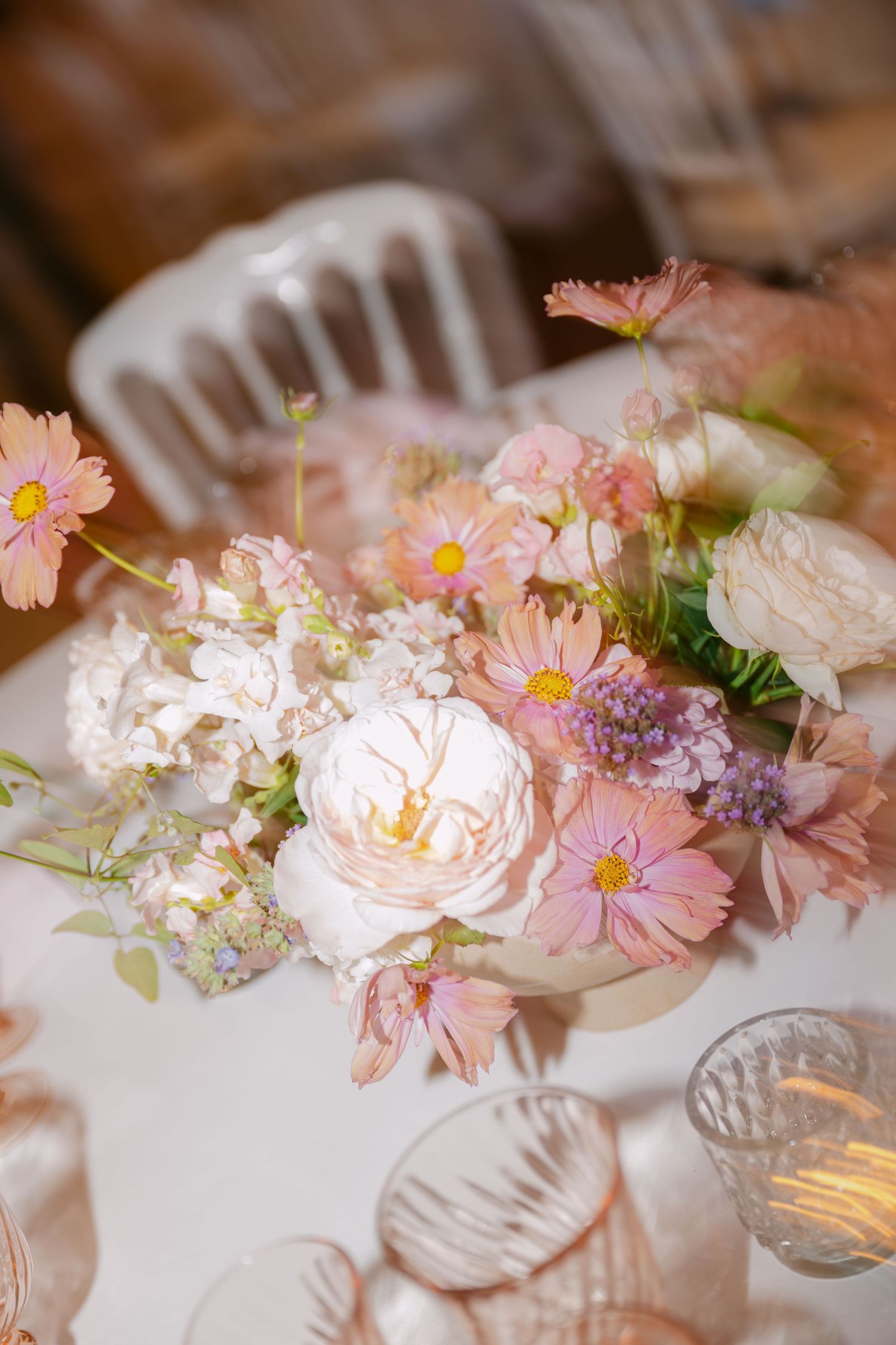 Close-up of a romantic wedding centerpiece featuring garden roses, cosmos, and wildflowers in soft pink and white tones.