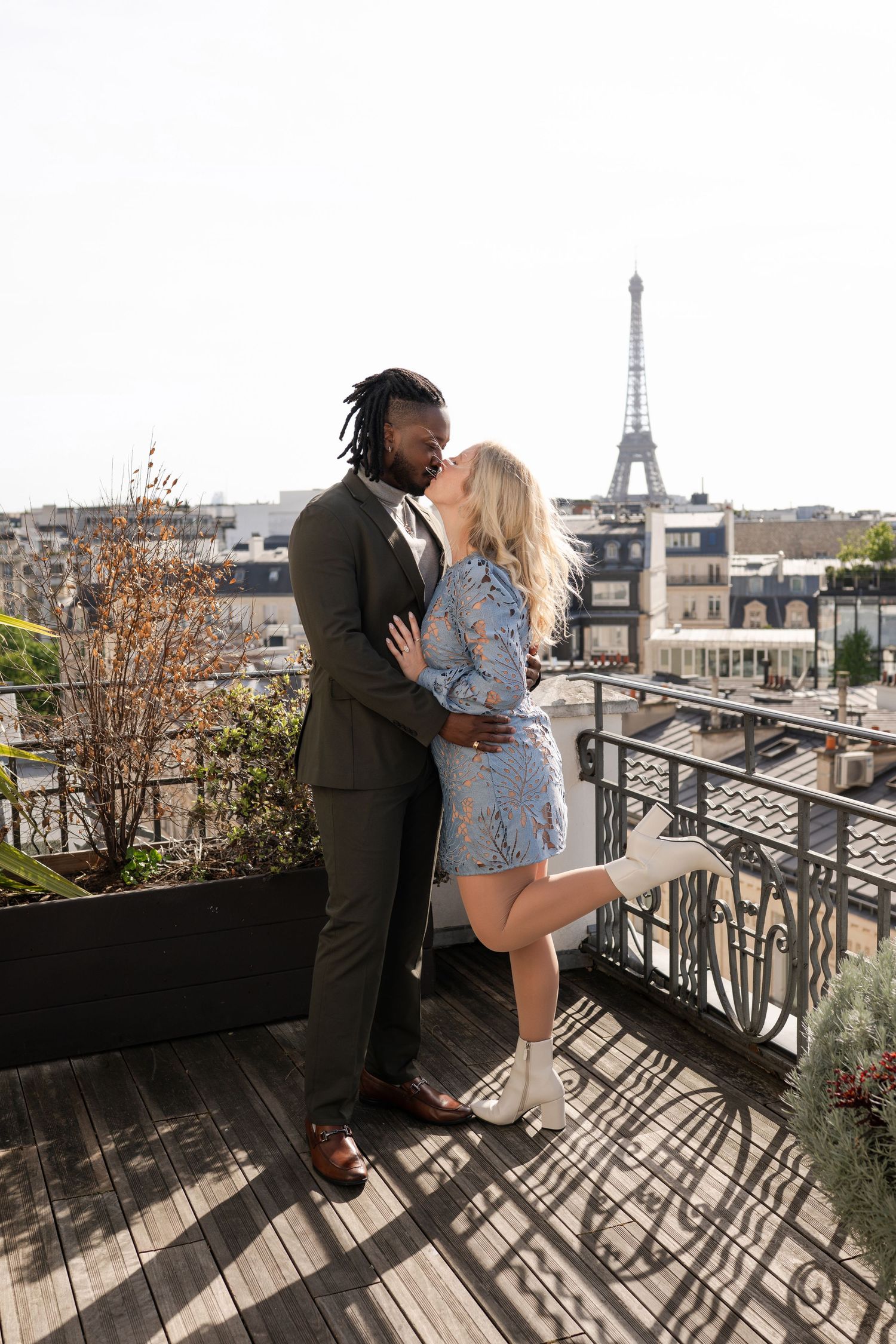 Couple kissing on a Parisian rooftop terrace with the Eiffel Tower in the background.
