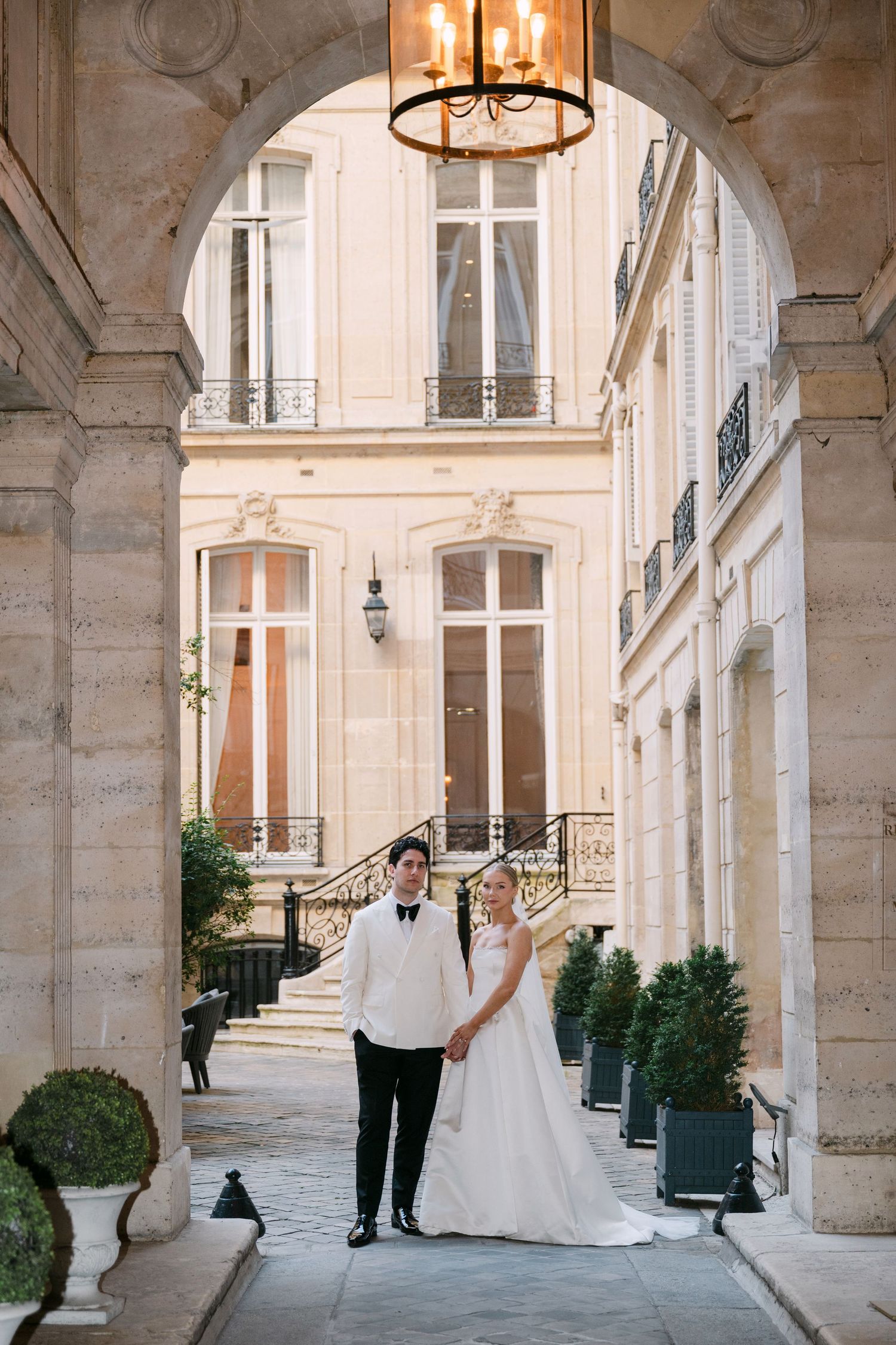 Bride and groom hold hands under an elegant stone archway at a classic Parisian courtyard wedding venue.