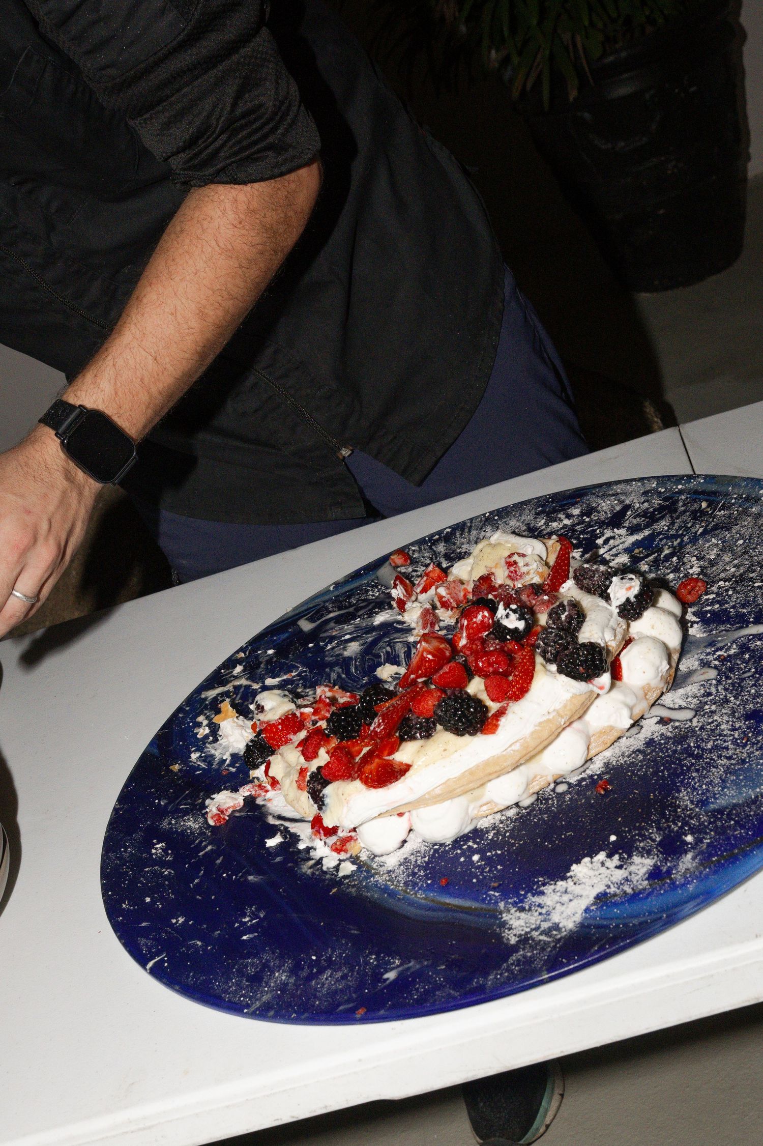 Close-up of elegant wedding cake topped with fresh berries and powdered sugar on blue platter.