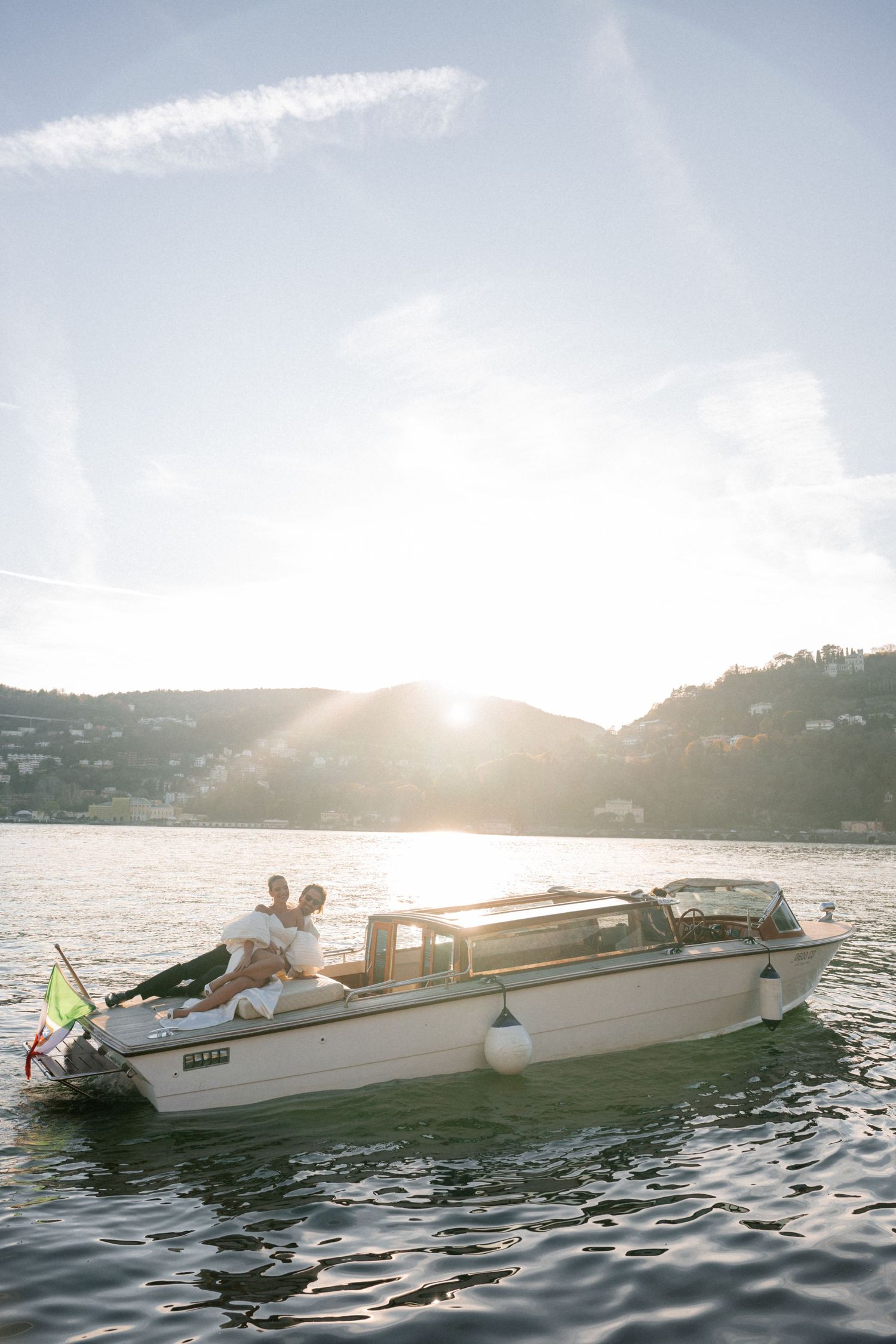 Newlyweds posing on a classic boat at sunset on Lake Como with golden light reflecting on water.
