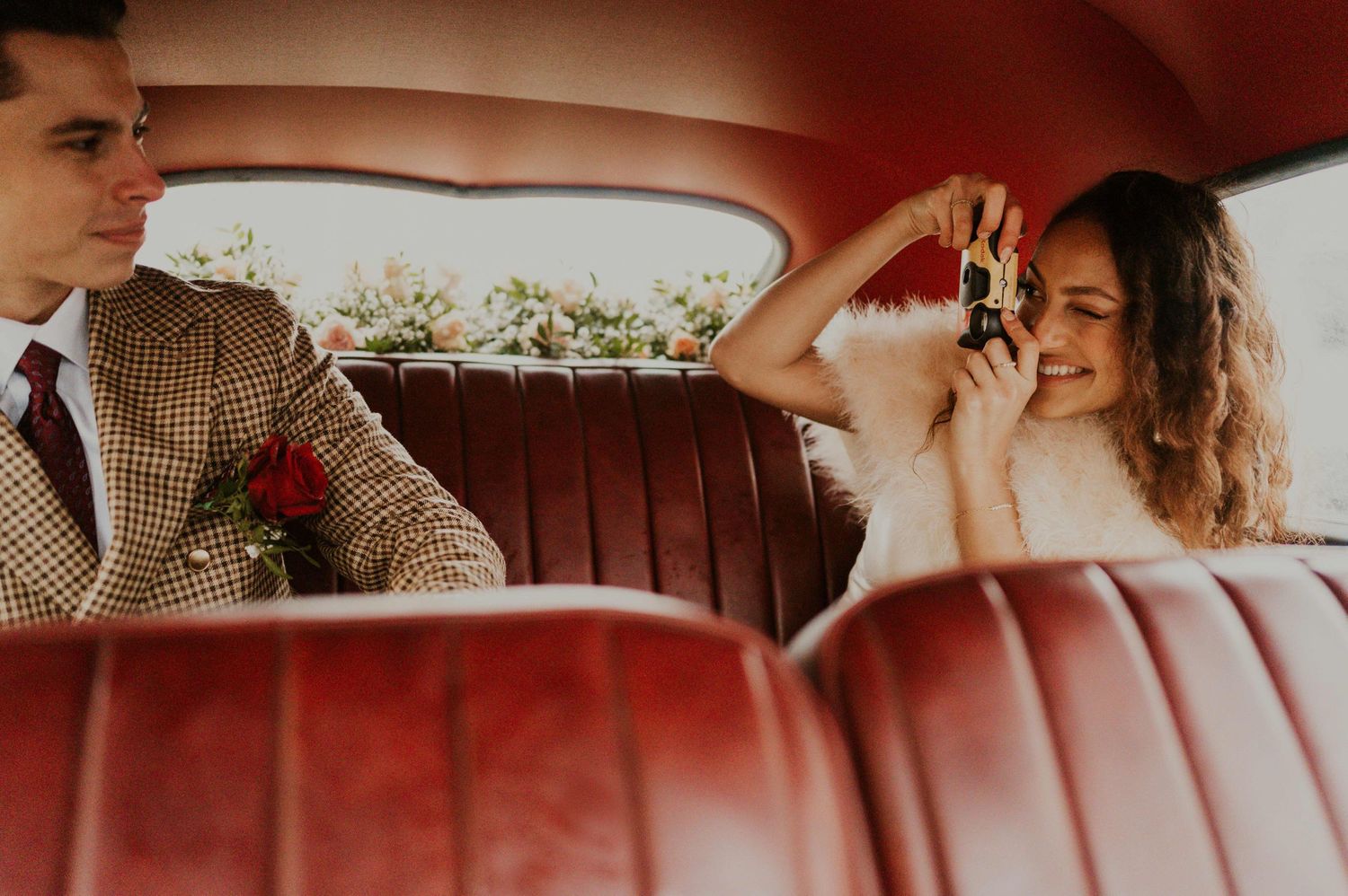 A couple shares a playful moment in the red leather interior of a vintage car.