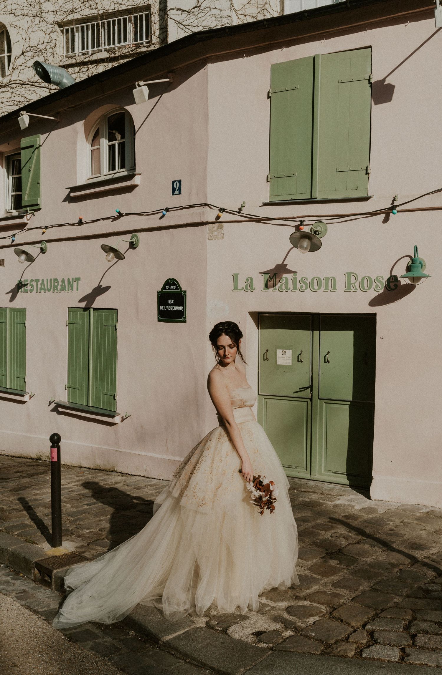 A dreamy bridal photo outside La Maison Rose restaurant with mint green shutters in Paris.