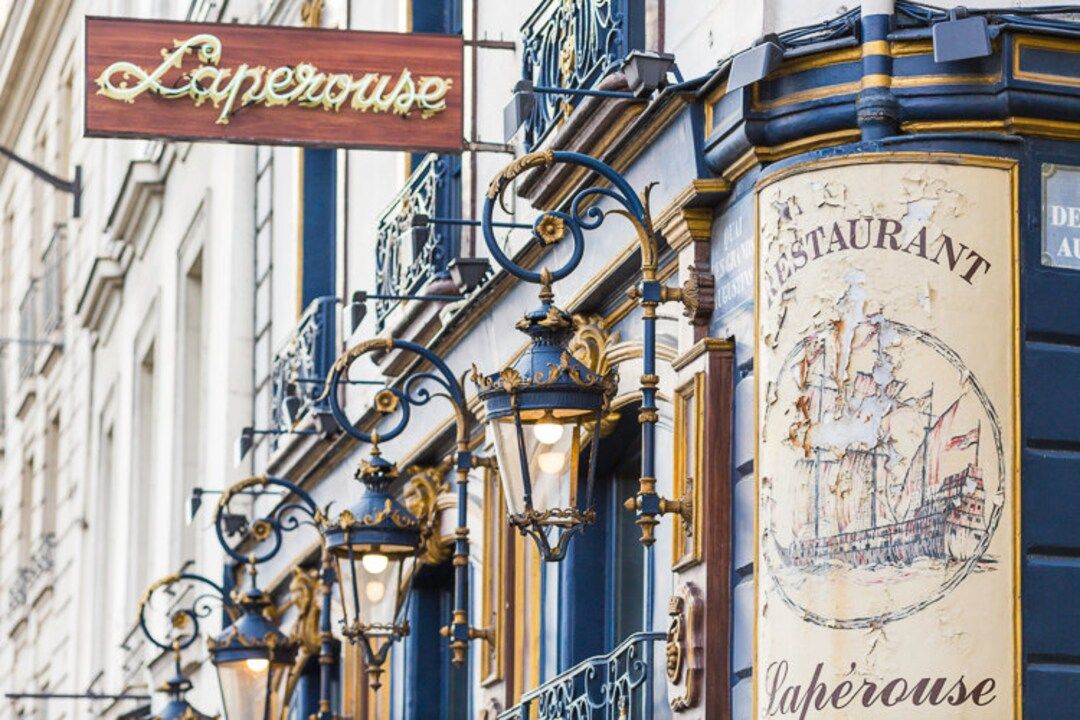Ornate vintage restaurant sign and Art Nouveau style lighting fixtures on Parisian building facade.