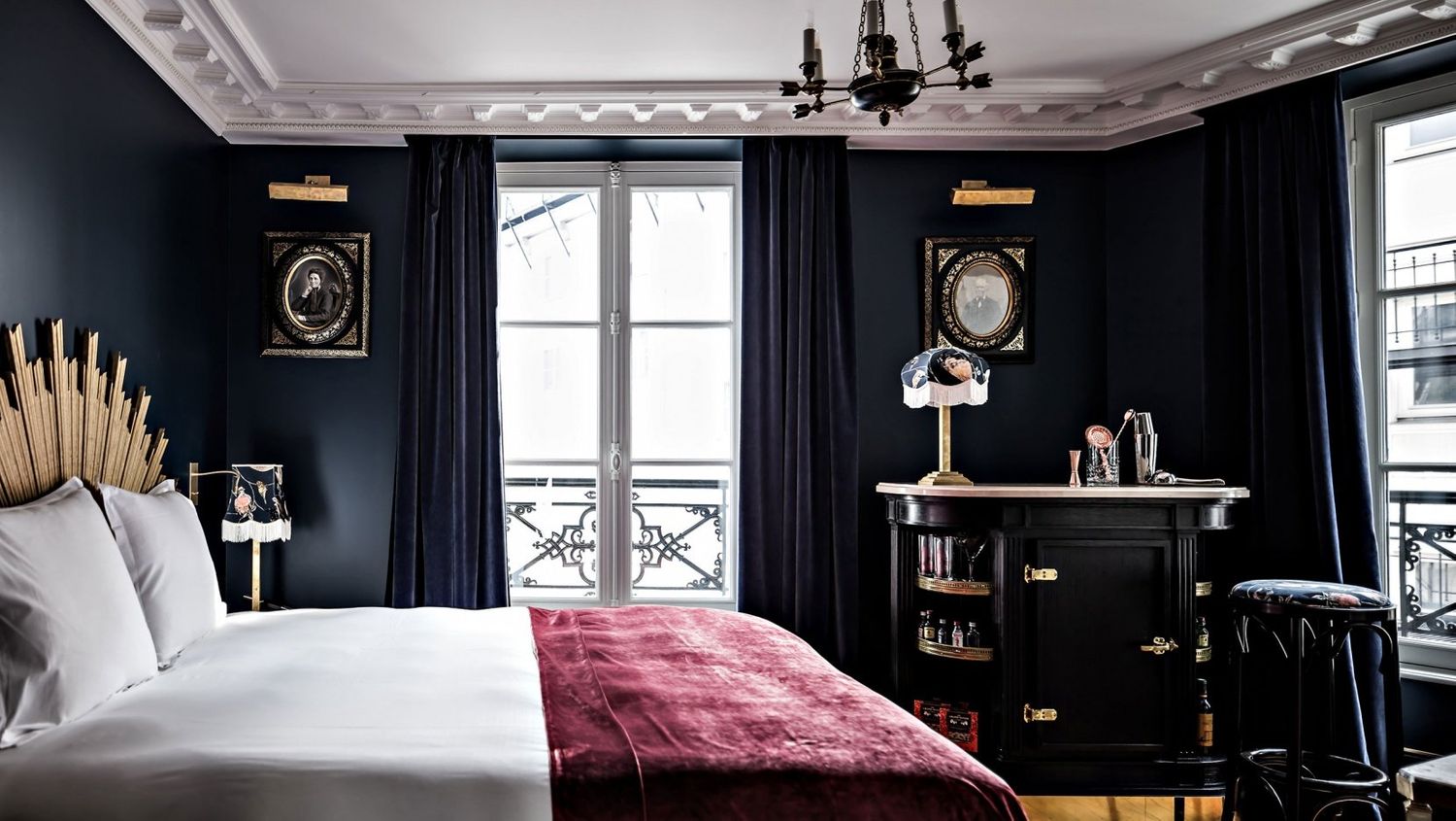 Sophisticated dark navy hotel bedroom with burgundy accents, French windows, and elegant vintage furnishings.