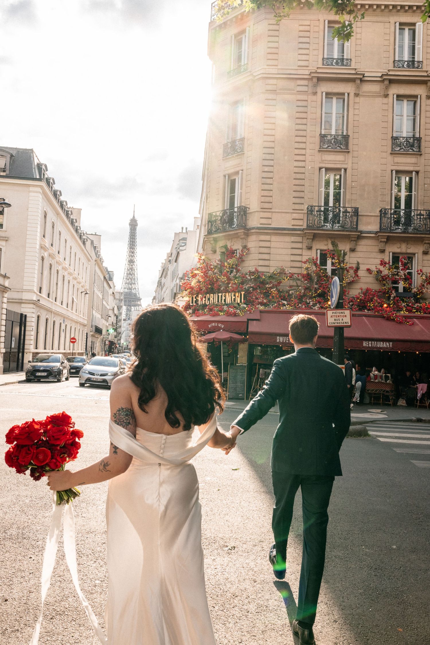 Couple walking down a romantic Parisian street with red roses and the Eiffel Tower visible in the distance.