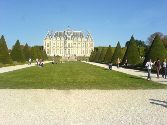 Manicured French chateau with symmetrical gardens and pathway leading to grand mansion.