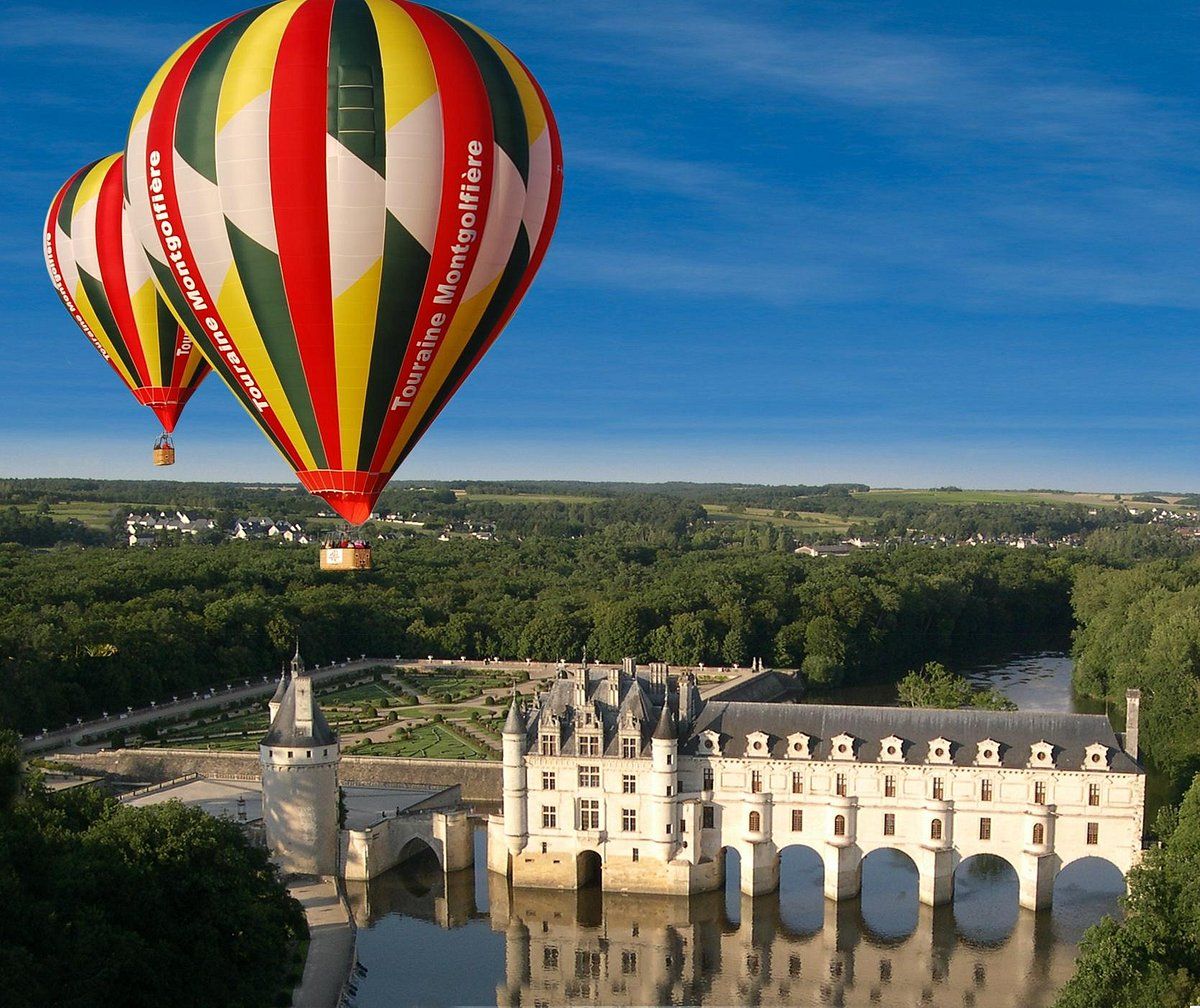 Colorful hot air balloon floating above Chenonceau castle spanning a river in France.