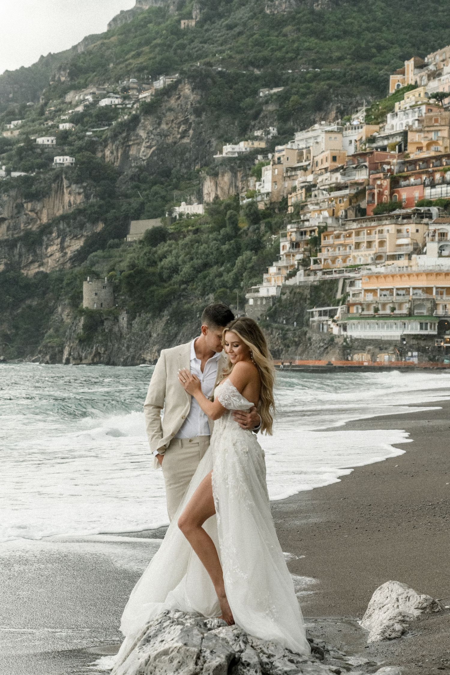 A romantic beachside moment captured against the dramatic backdrop of Positano's hillside architecture.