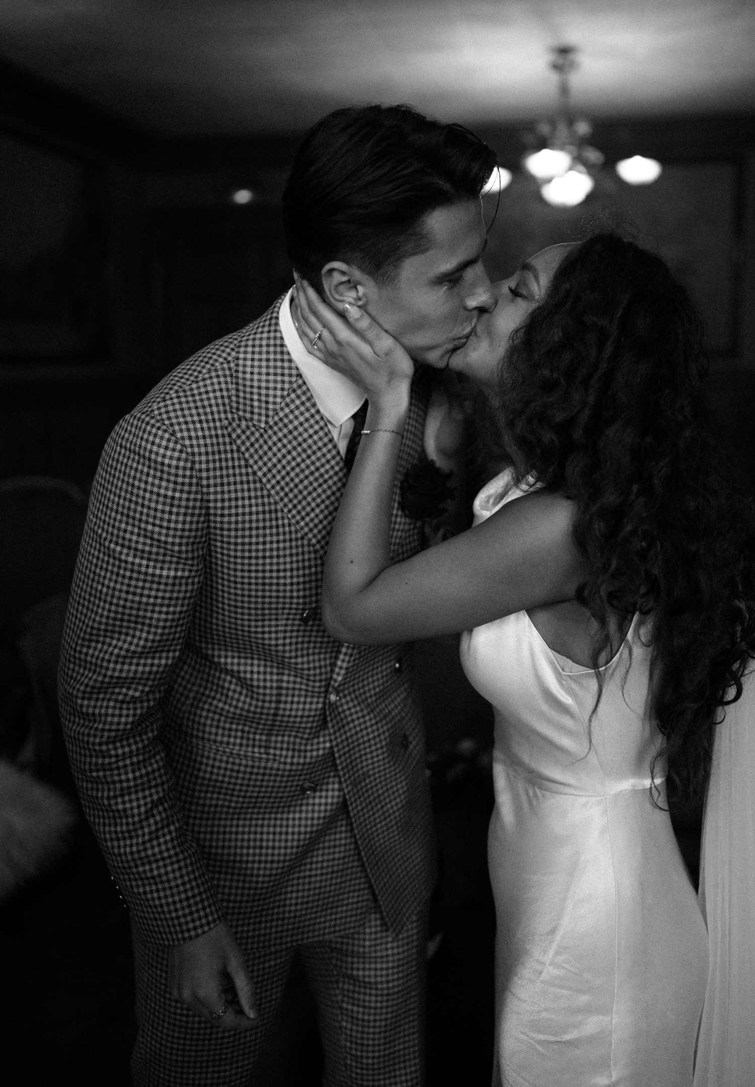 An intimate black and white portrait of a couple sharing their first kiss as newlyweds.