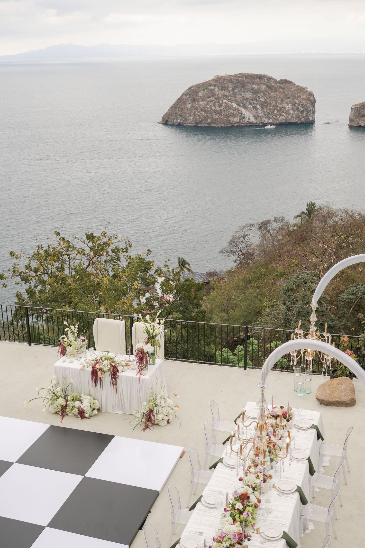 Elegant outdoor wedding reception on a terrace overlooking the ocean, featuring floral centerpieces and a checkered dance floor.