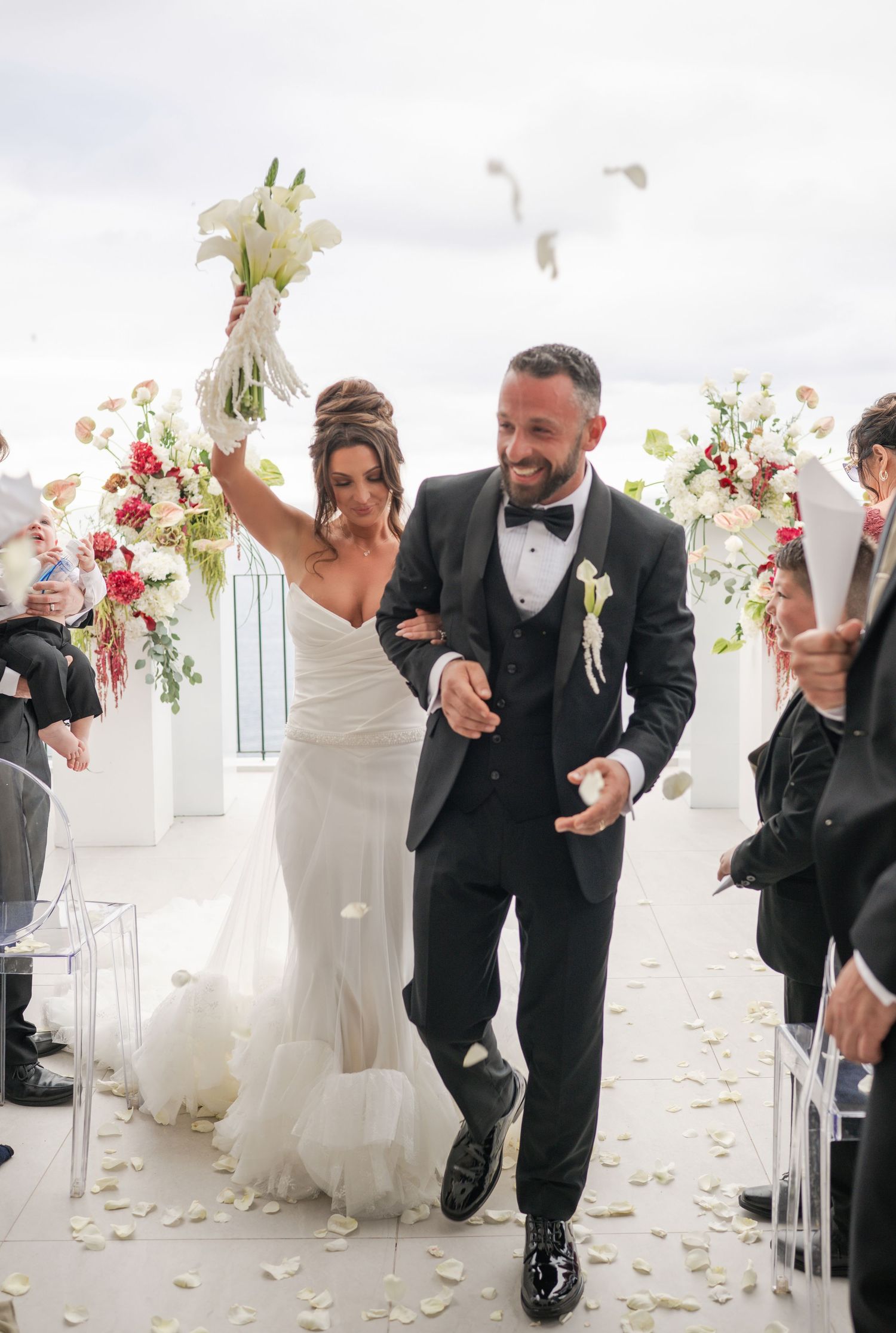 Joyful newlyweds celebrate recessional as bride raises bouquet and white doves fly overhead.
