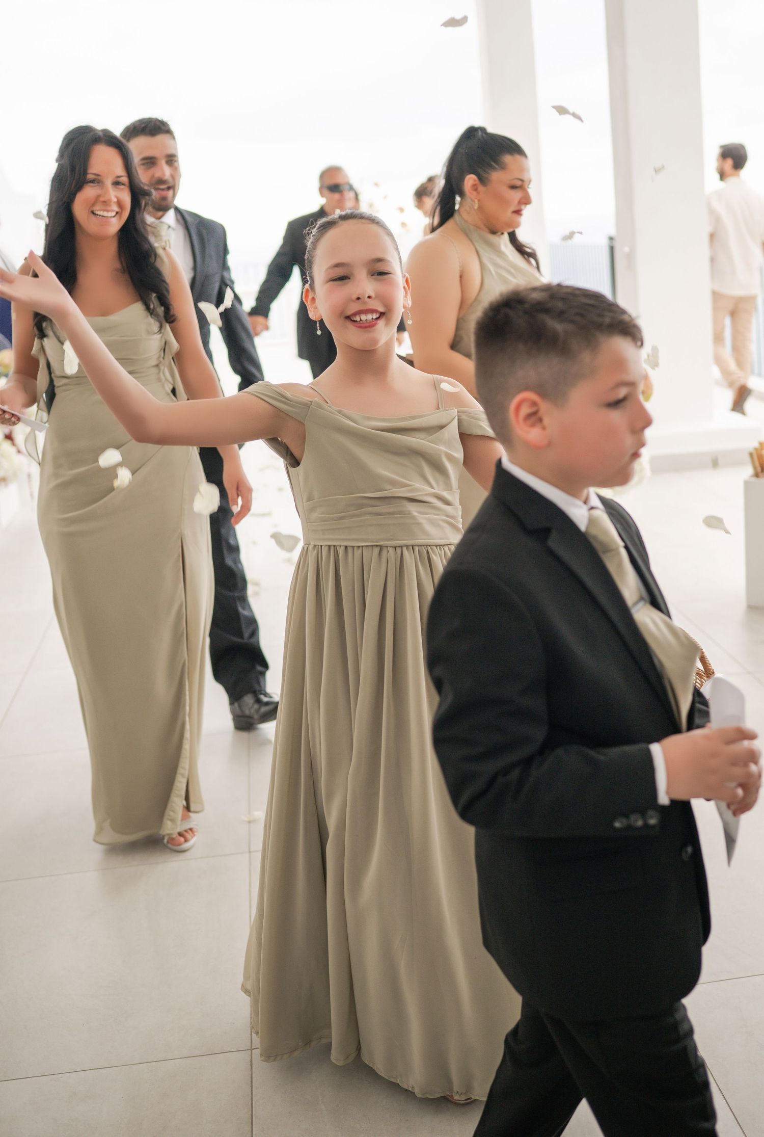 Young flower girl in gold dress smiles during wedding reception procession with bridesmaids and ring bearer.