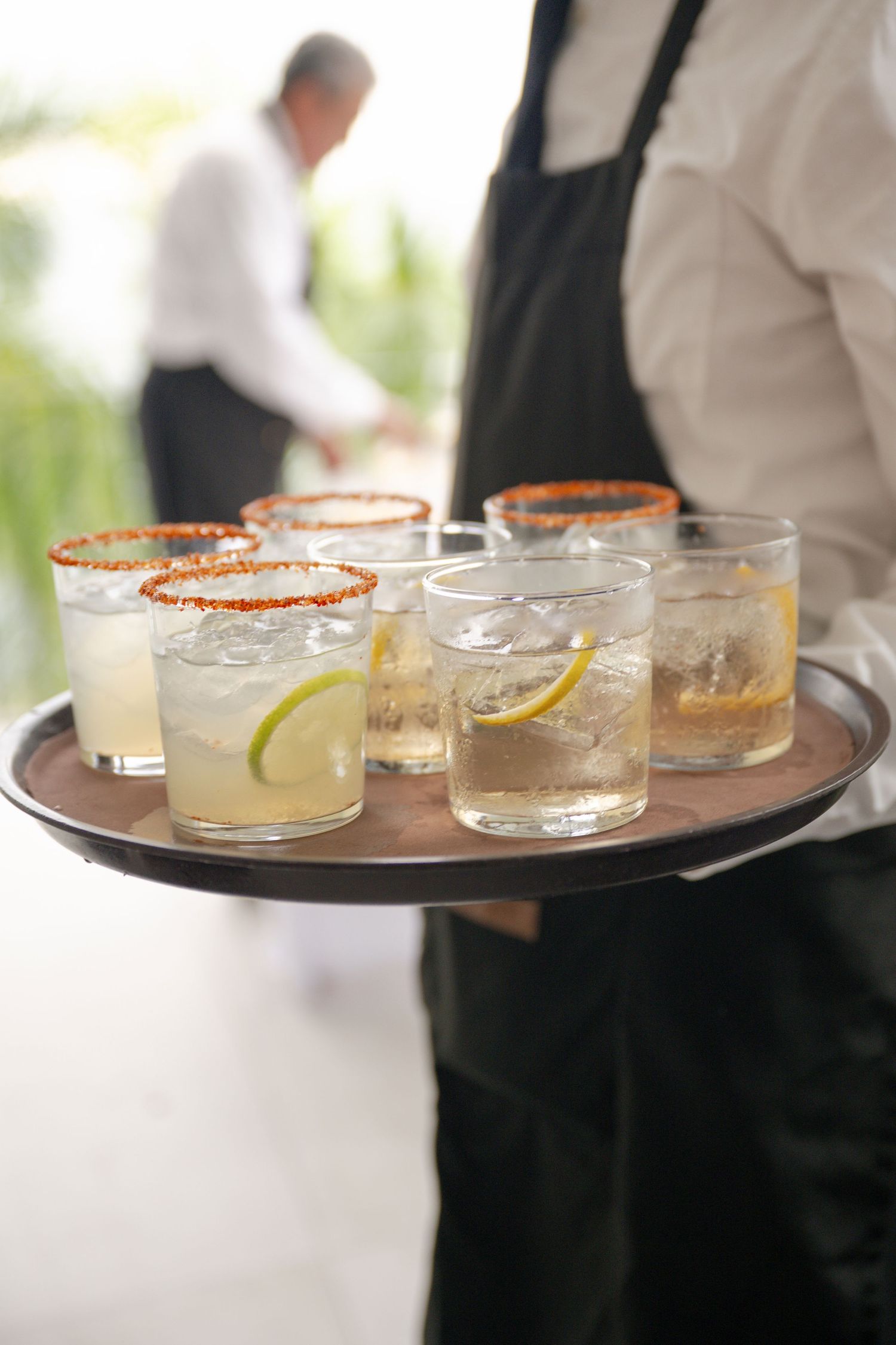 Waiter serving tray of cocktails with lime garnish and chili salt rims at an elegant catered event.