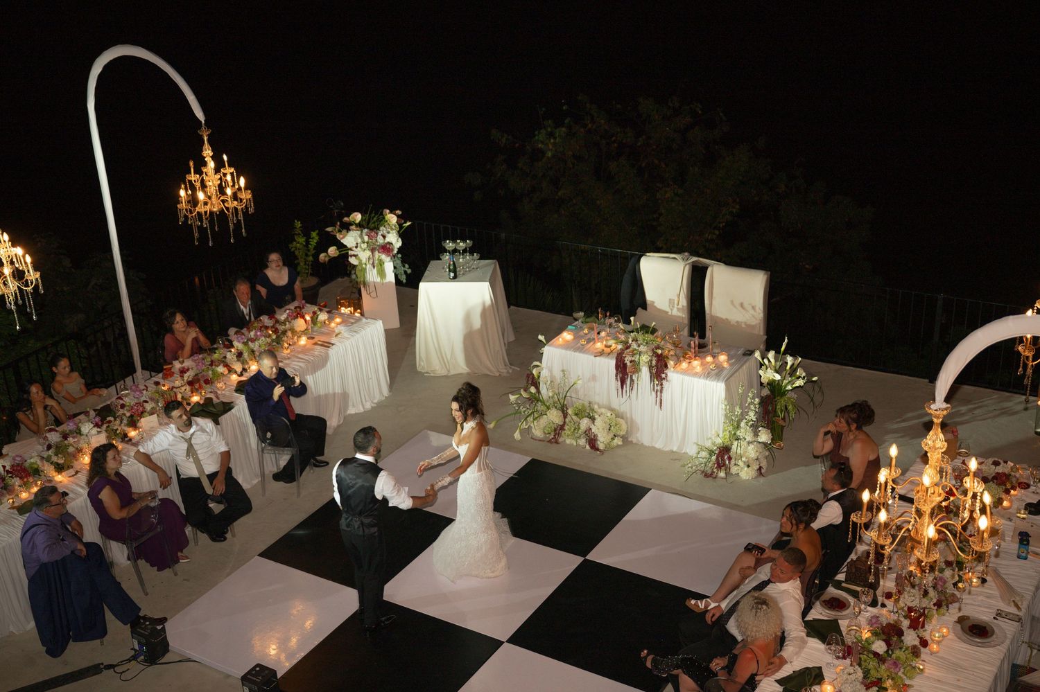 Elegant outdoor wedding reception at night with checkered dance floor, candlelit tables, and bride and groom sharing a dance.