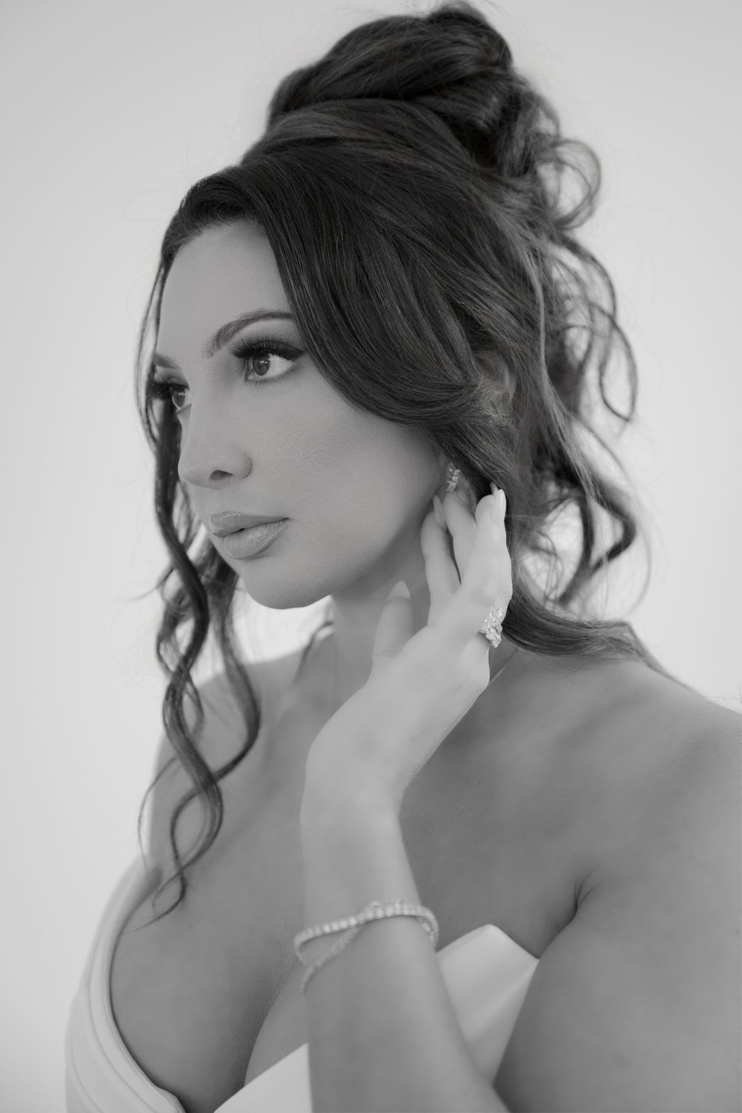 Elegant black and white portrait of a bride with updo hairstyle touching her pearl earring gracefully.