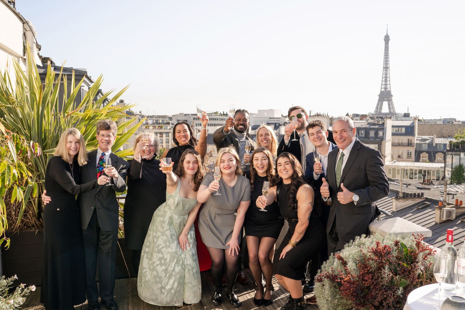 Group celebrating on a Paris rooftop terrace with the Eiffel Tower in the background on a sunny day.