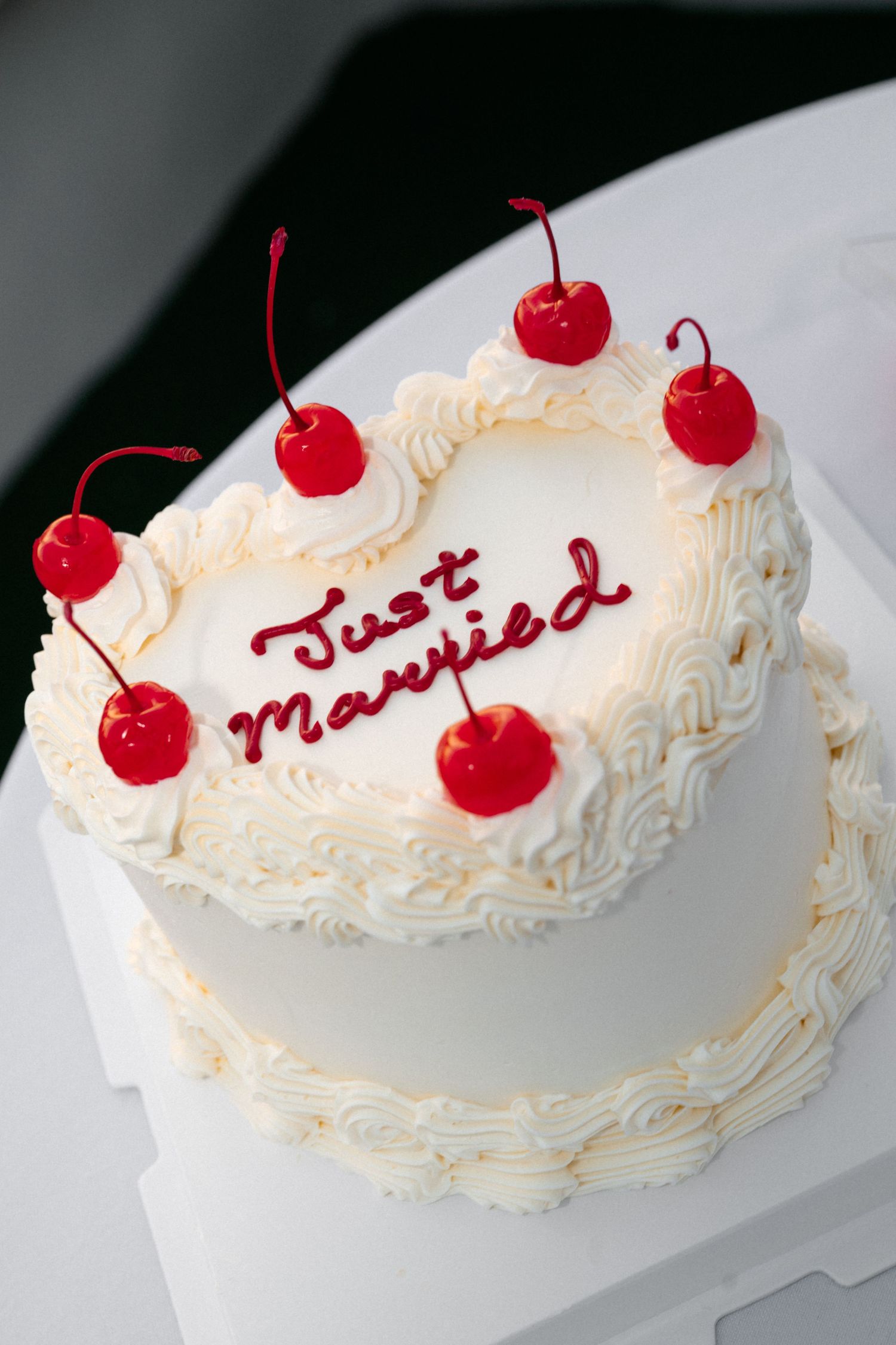 A white wedding cake decorated with whipped cream frosting and bright red maraschino cherries on top.
