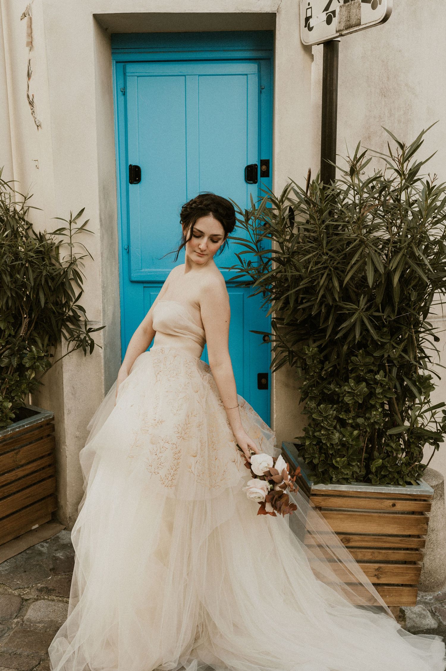A bridal portrait featuring a flowing tulle gown against a bright blue door and potted plants.