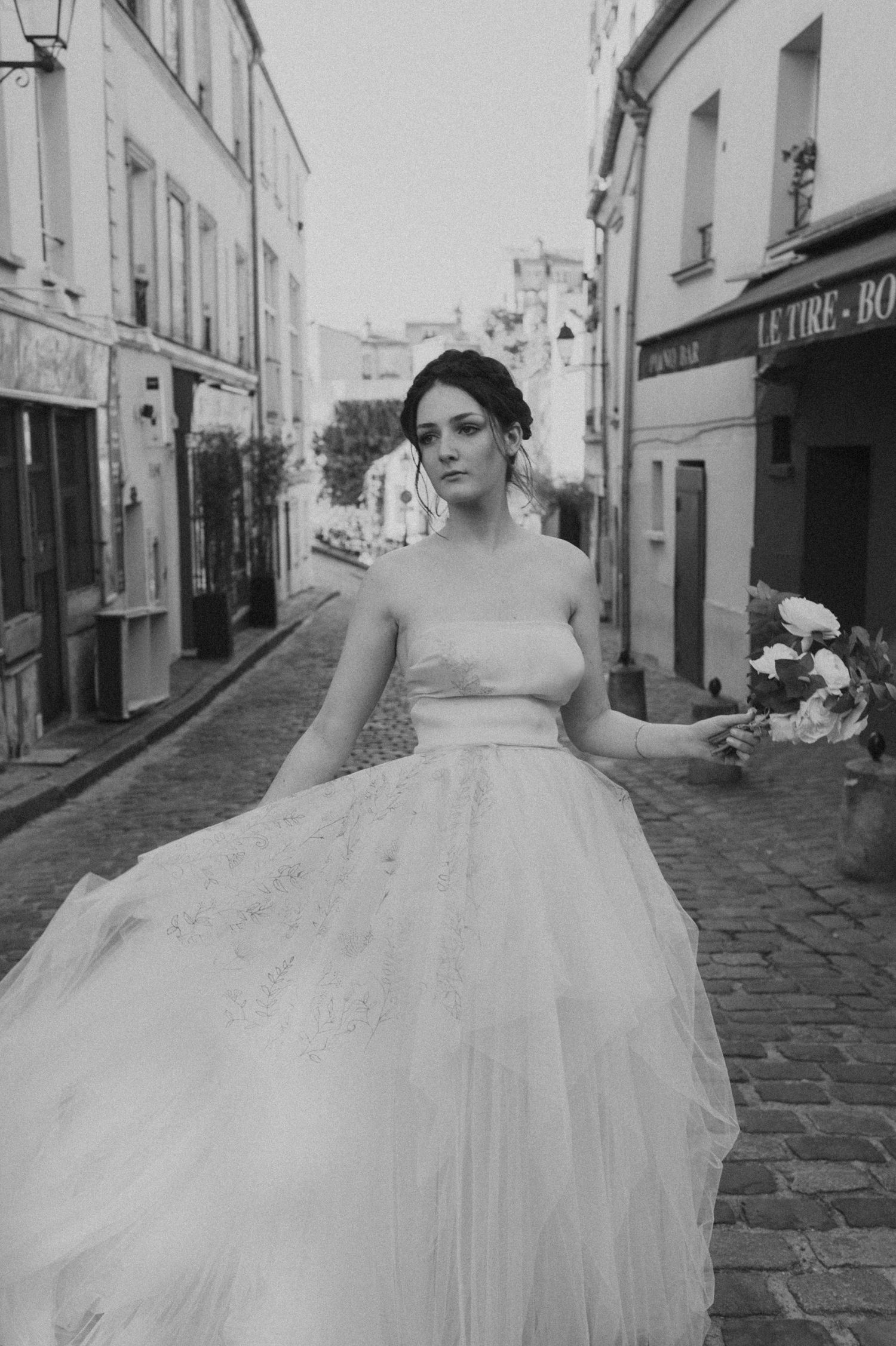 Black and white portrait of bride in strapless gown on Parisian cobblestone street.