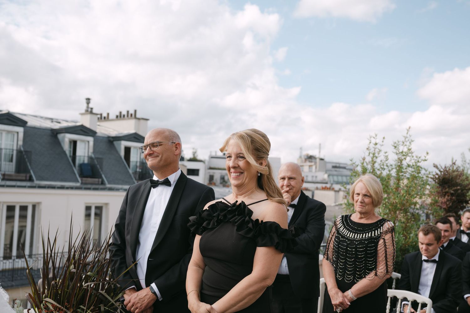 Wedding party gathers on an outdoor terrace for formal group photos on a sunny afternoon.
