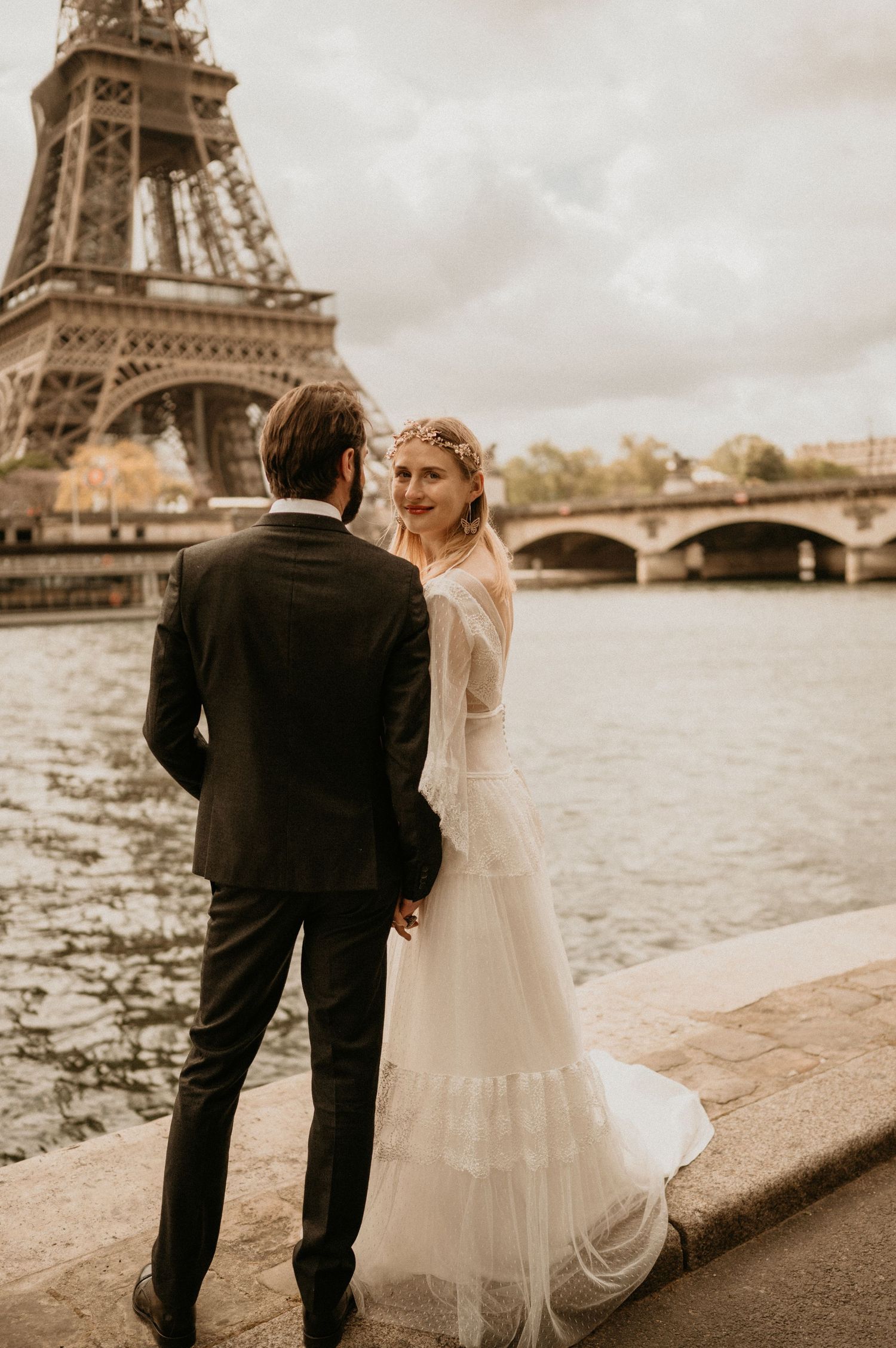 A romantic wedding photo by the Seine River in Paris with the Eiffel Tower and bridge in the background.