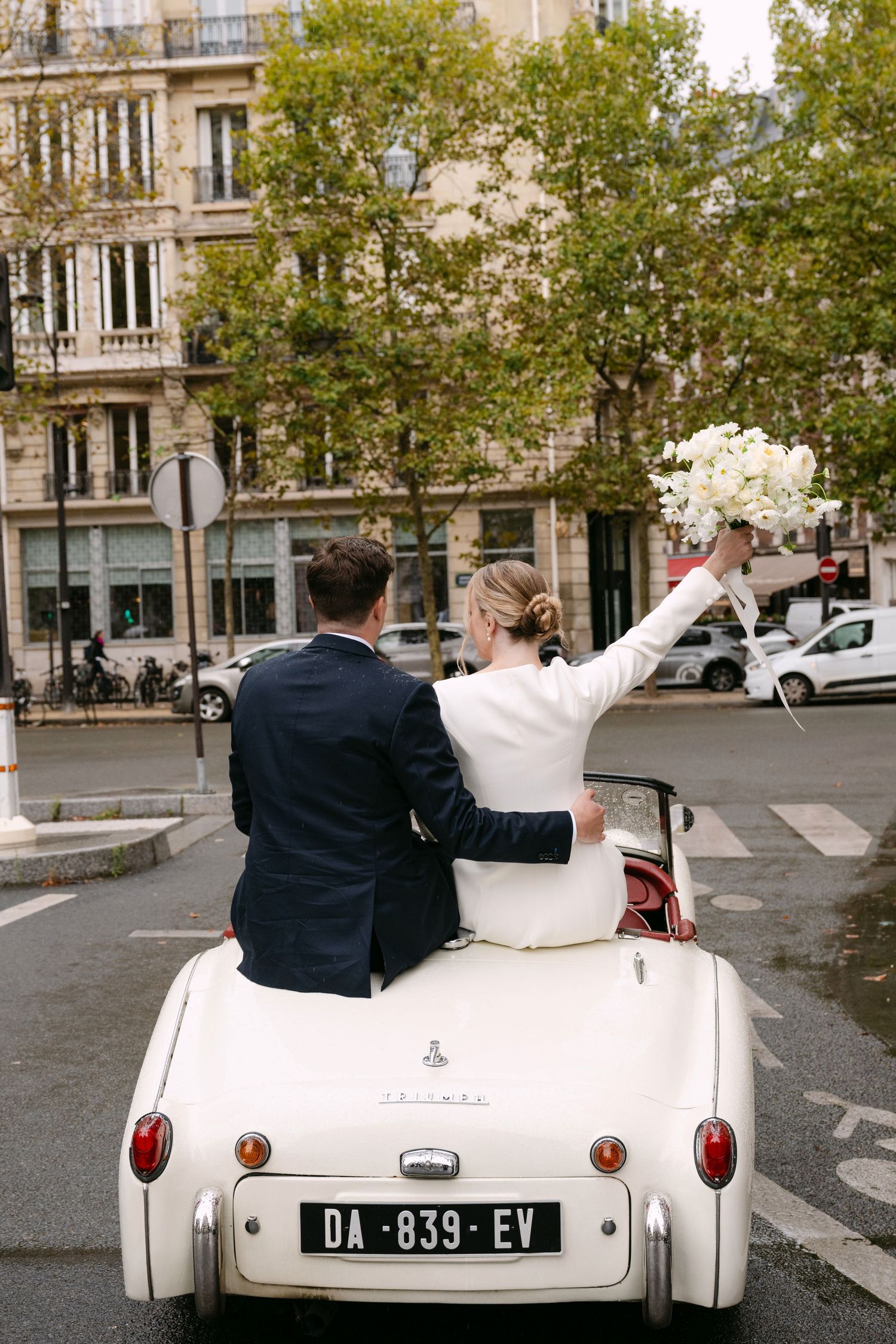 Newlyweds ride in a classic white convertible car through the streets of Paris on their wedding day.