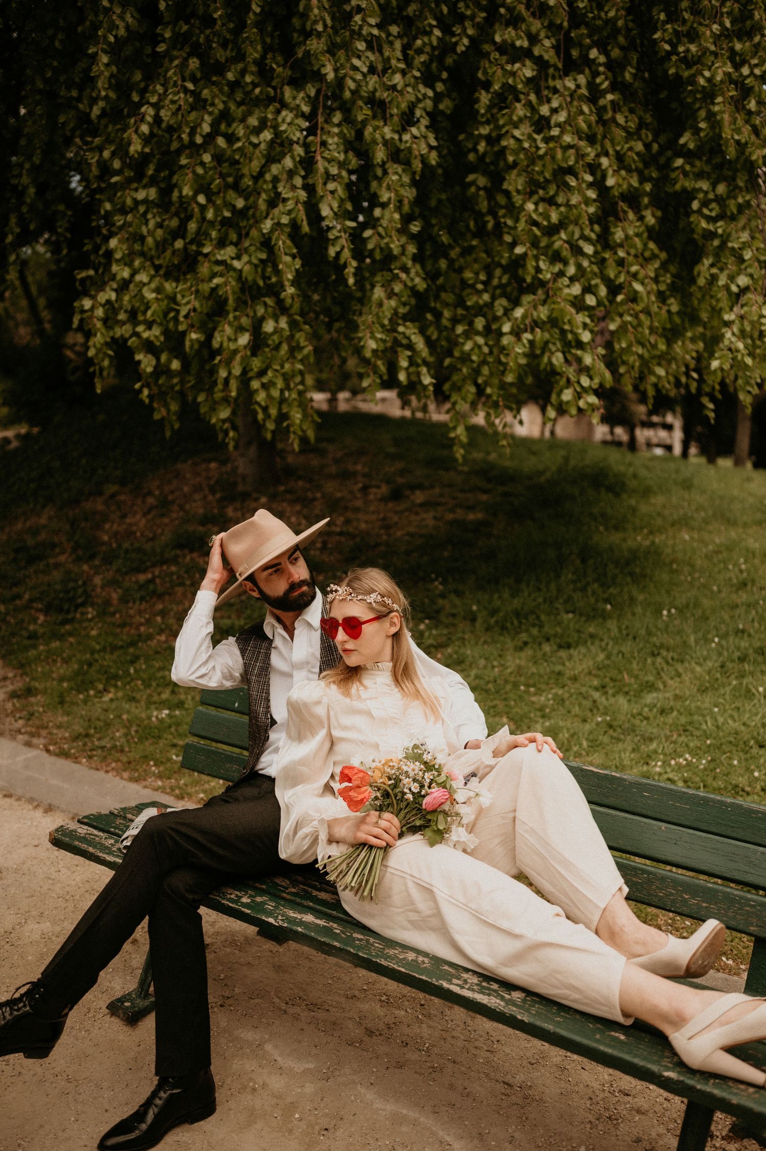Couple sharing intimate moment on park bench with floral bouquet and western hat.