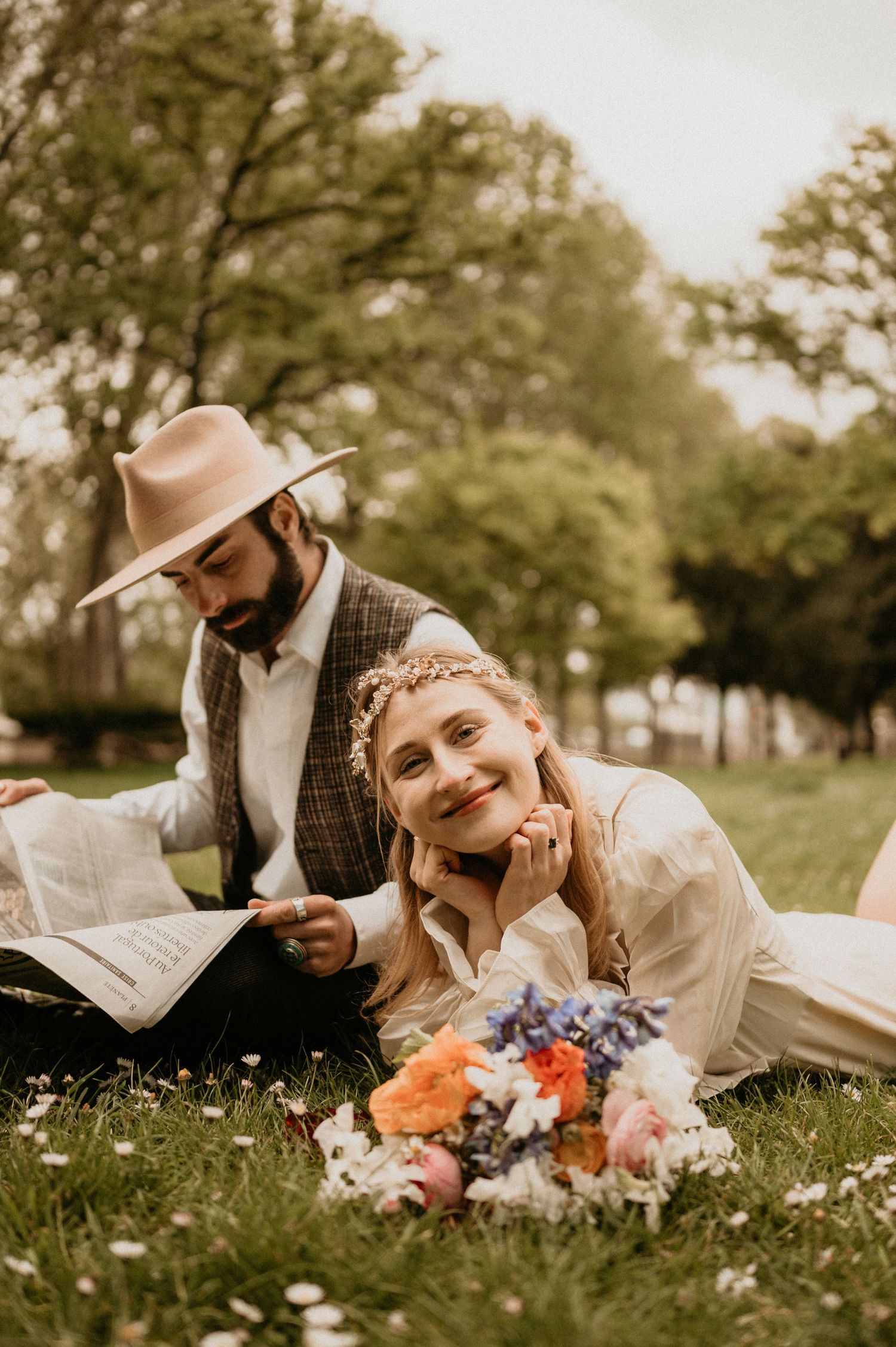 Romantic vintage-styled couple enjoying newspaper and flowers in spring park setting.