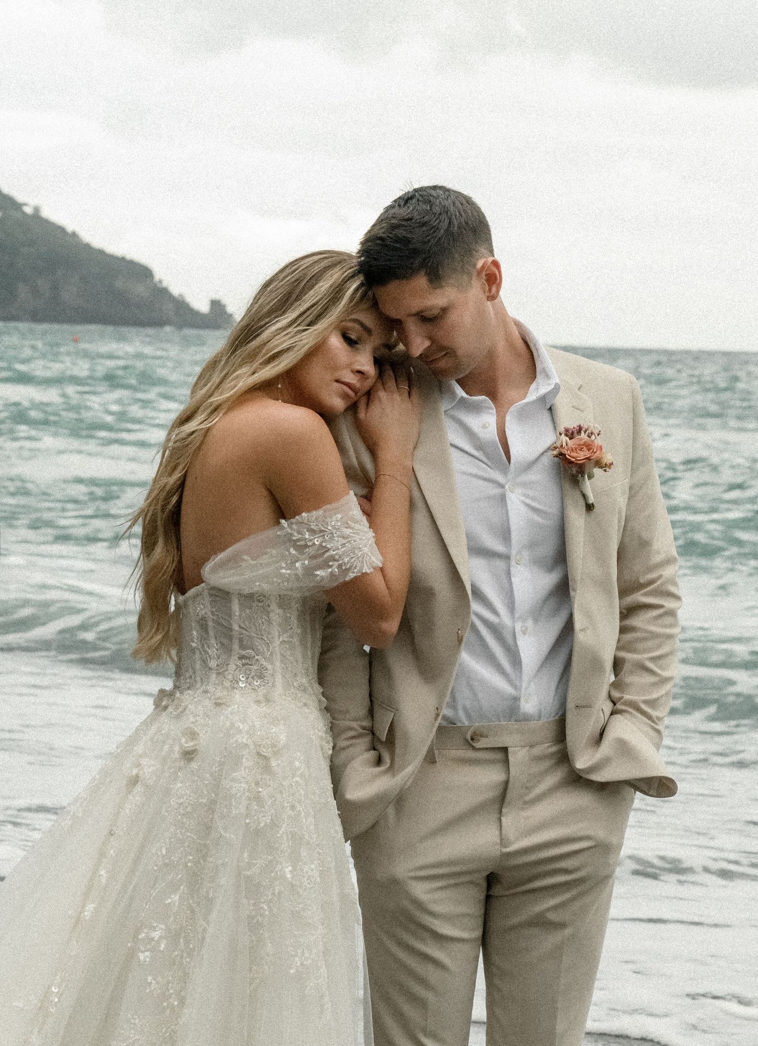 A couple in formal attire shares an intimate moment by the ocean on their wedding day.