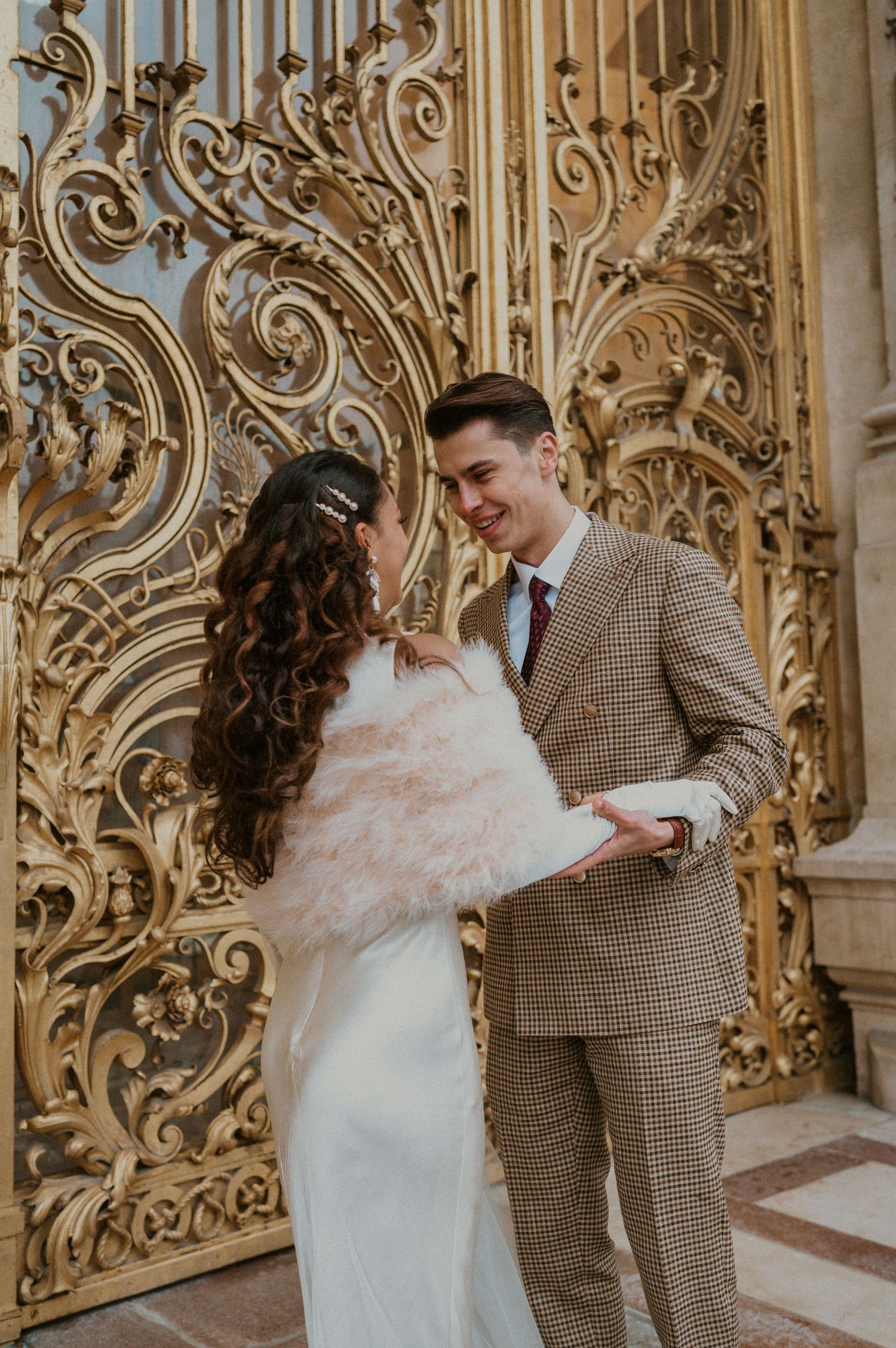 Elegant wedding couple laughing together against ornate gold architectural details.