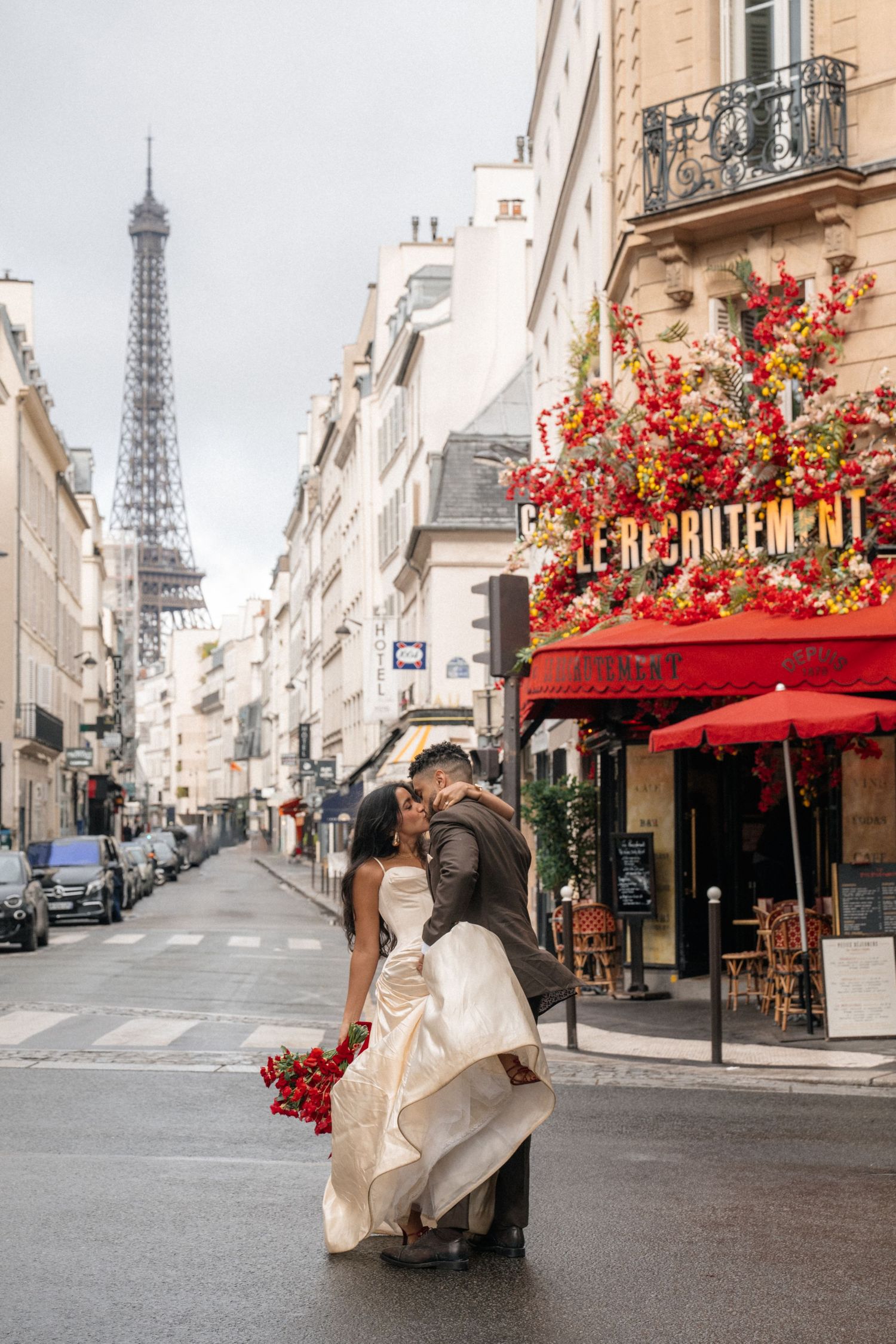 Wedding couple kissing on a Paris street with the Eiffel Tower in the background.