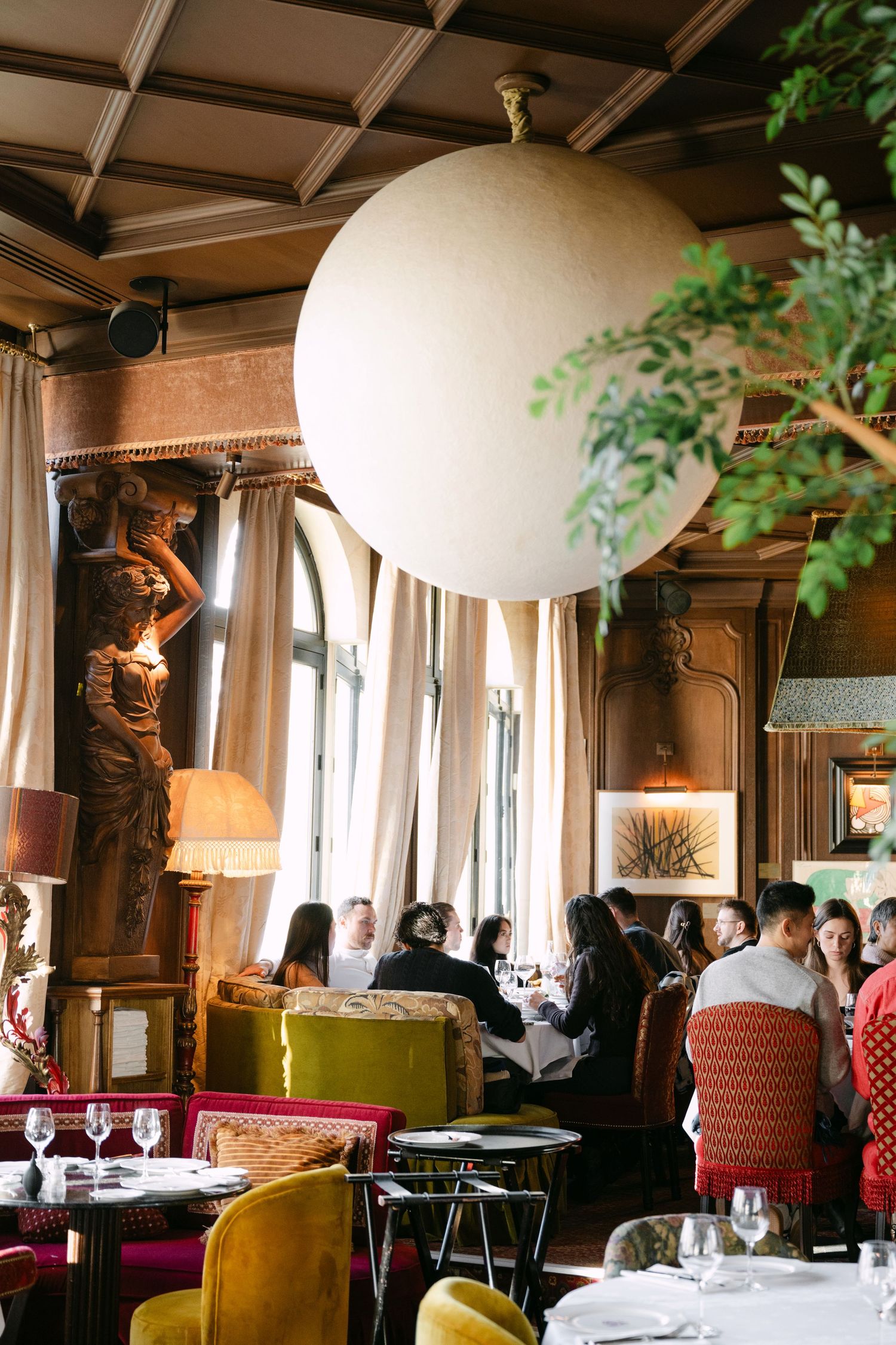 Luxurious Parisian restaurant interior with large globe pendant light and velvet chairs.
