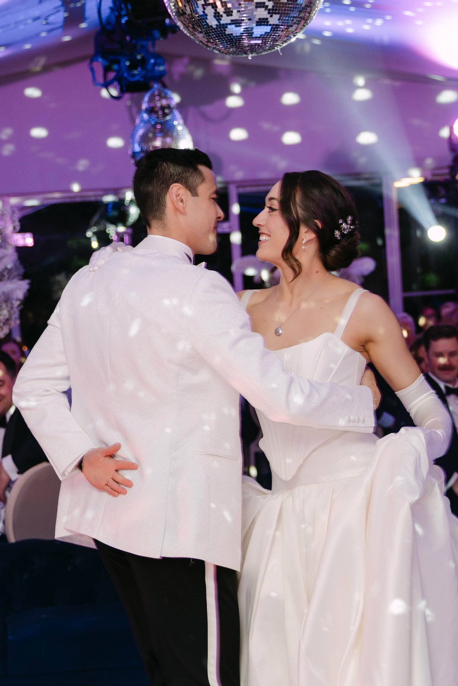 Bride in white gown and groom in white tuxedo share first dance at wedding reception.