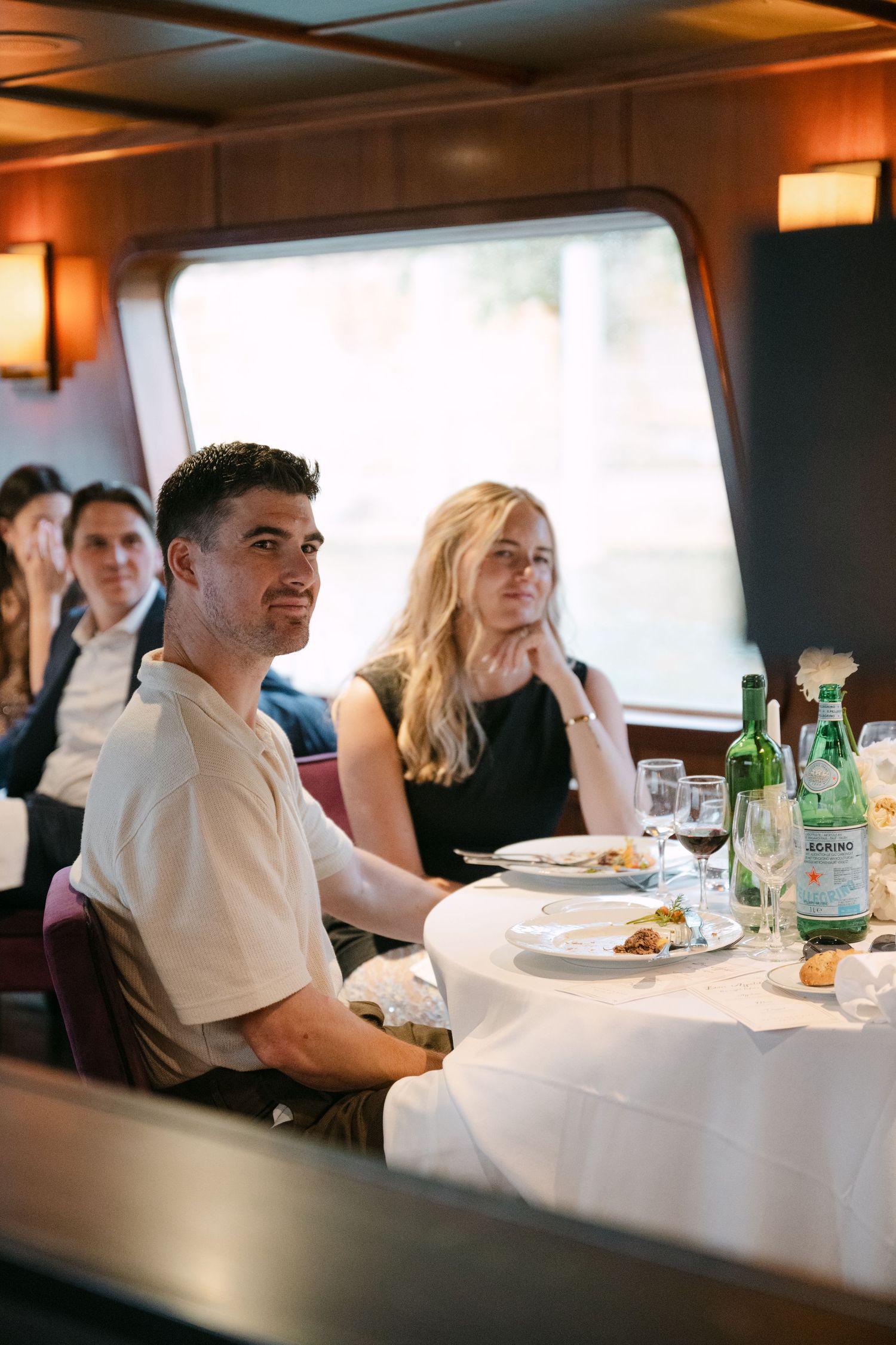 Wedding guests sit at an elegant white-clothed dining table aboard a luxury Seine River cruise boat.