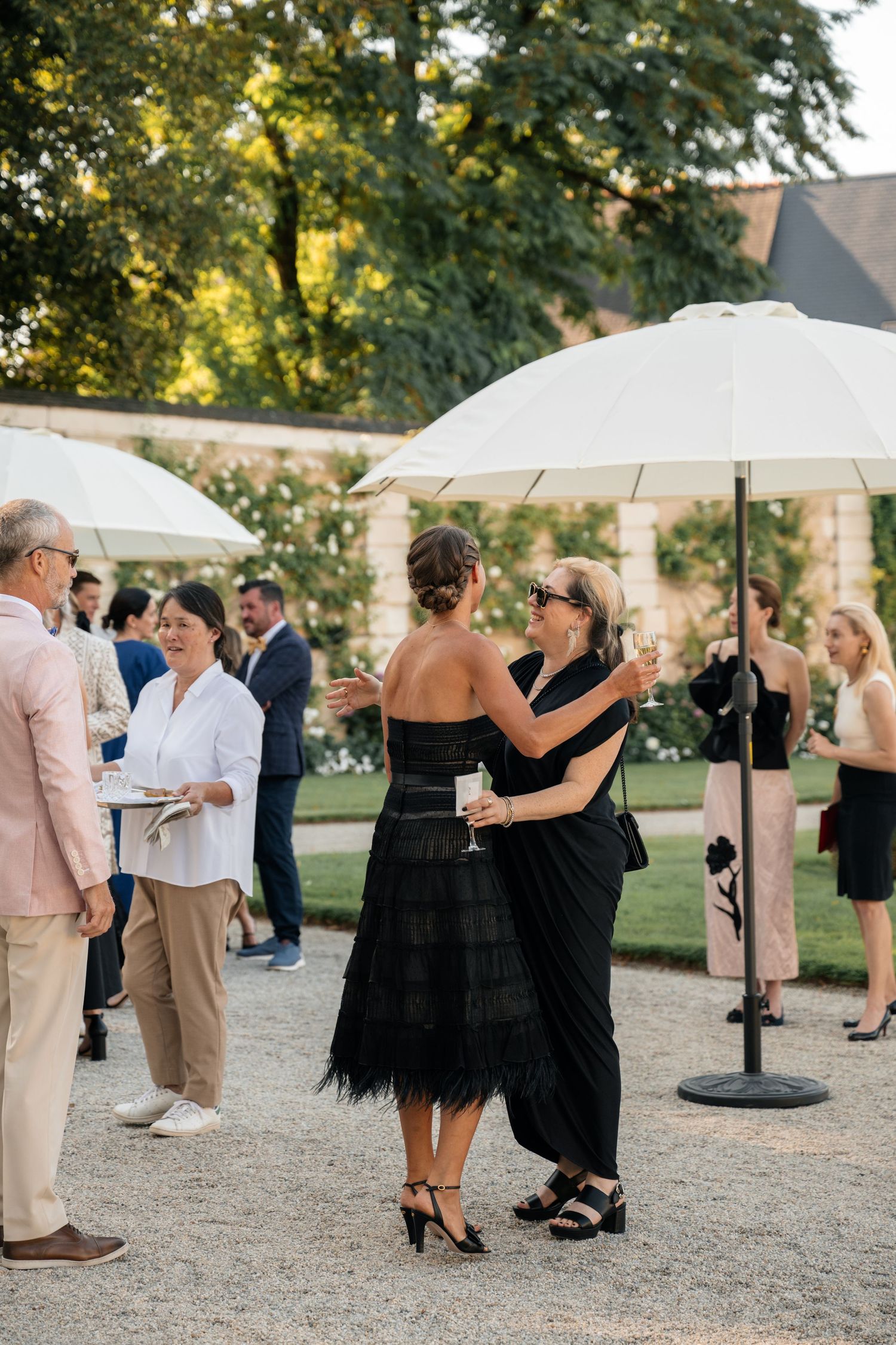 Guests in elegant attire mingling outdoors under white parasols at a sophisticated garden cocktail party.