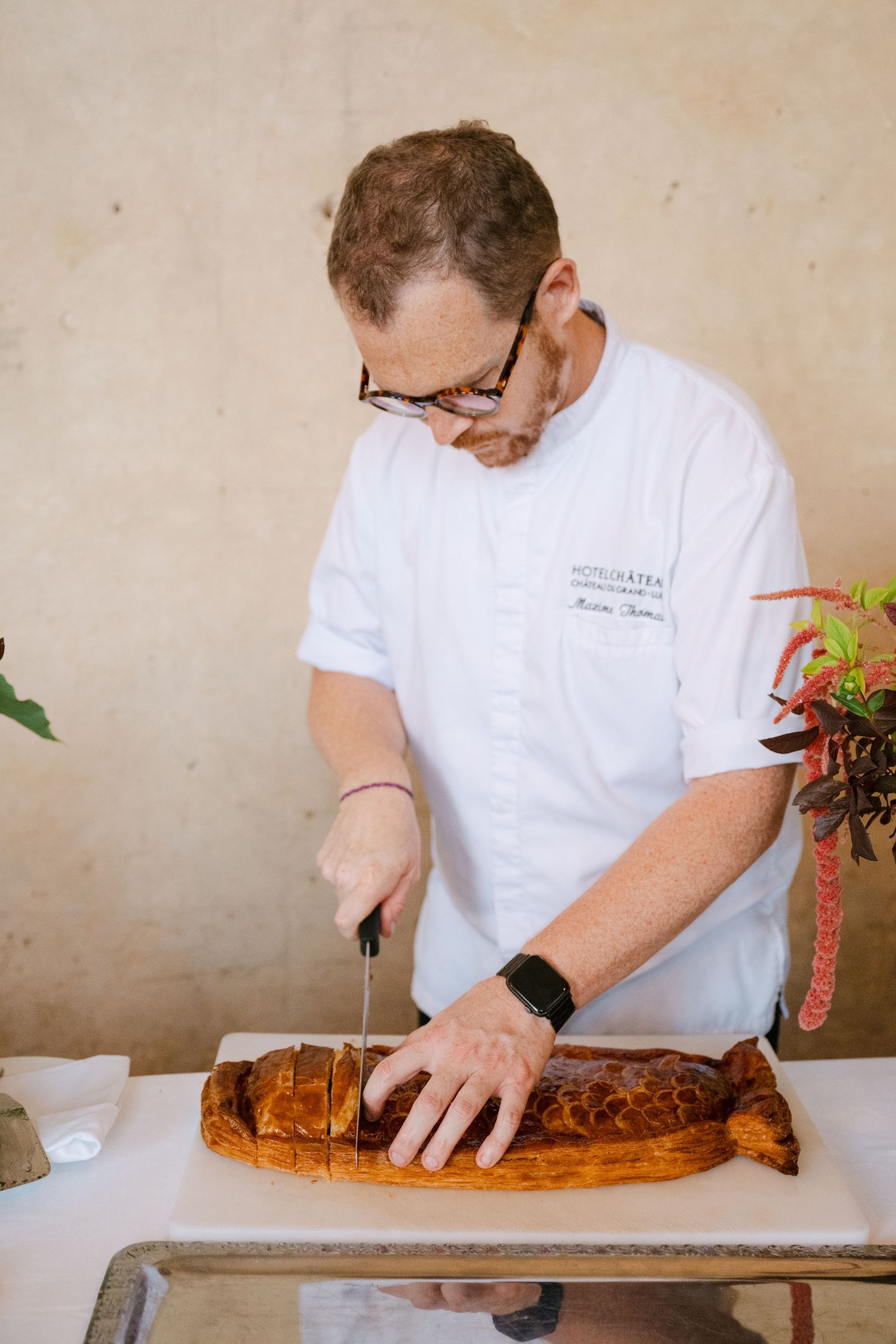 Chef in white uniform slicing freshly baked decorative bread at a wedding catering.