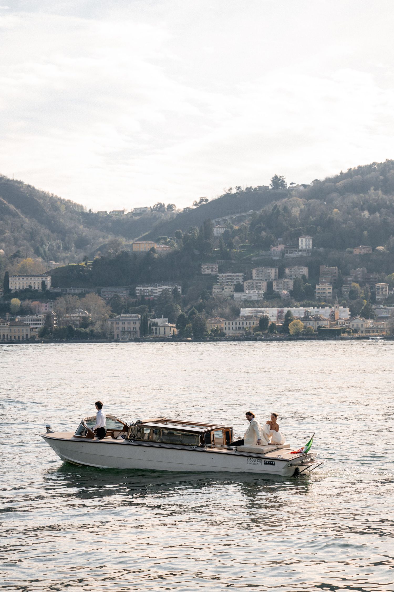 Wedding couple riding a classic motorboat on Lake Como with scenic mountain backdrop.